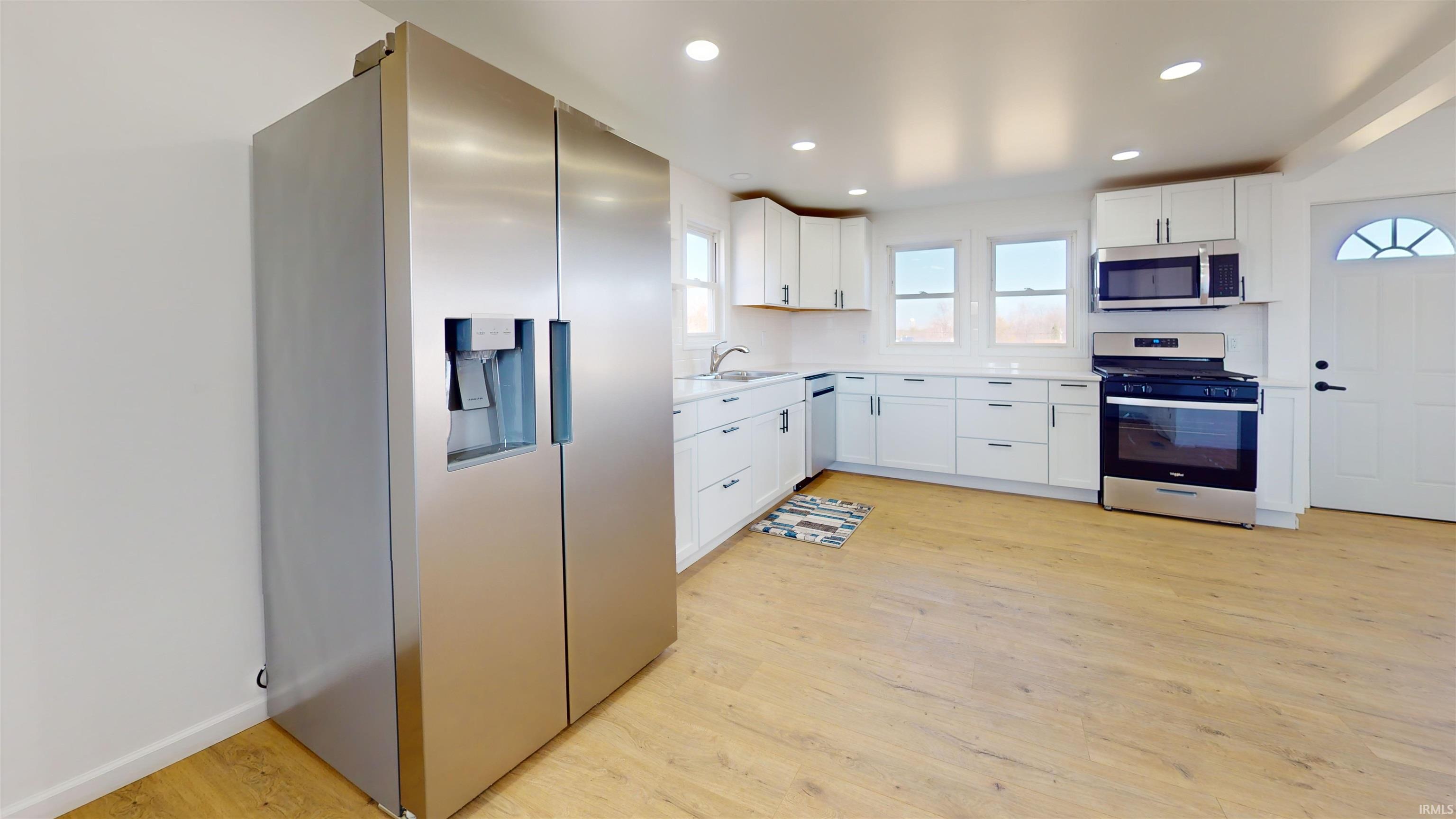 Kitchen featuring stainless steel appliances, light countertops, recessed lighting, white cabinetry, and light wood-type flooring