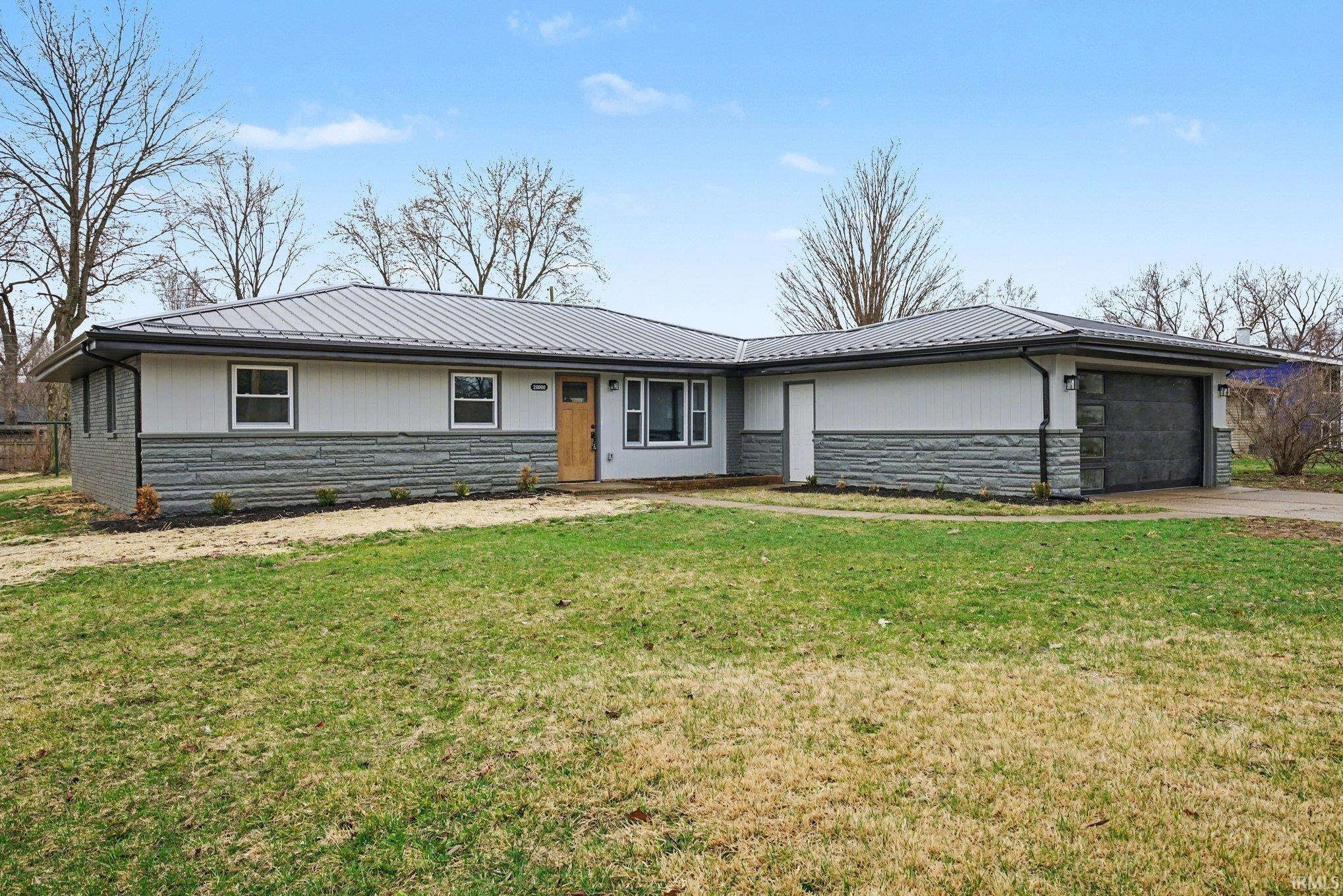 Single story home with stone siding, a garage, a front lawn, and a metal roof