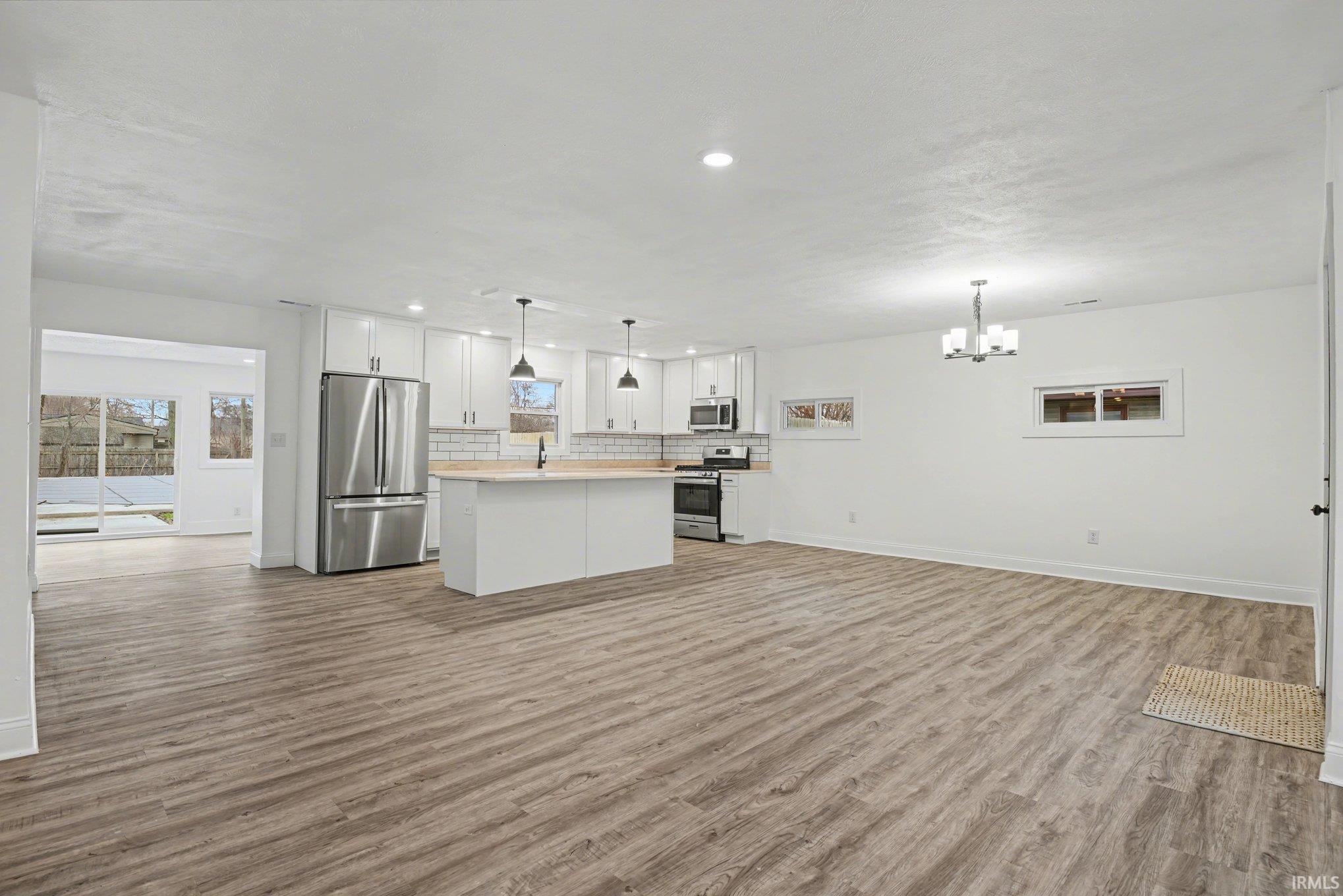 Kitchen with open floor plan, stainless steel appliances, light countertops, white cabinets, and a center island