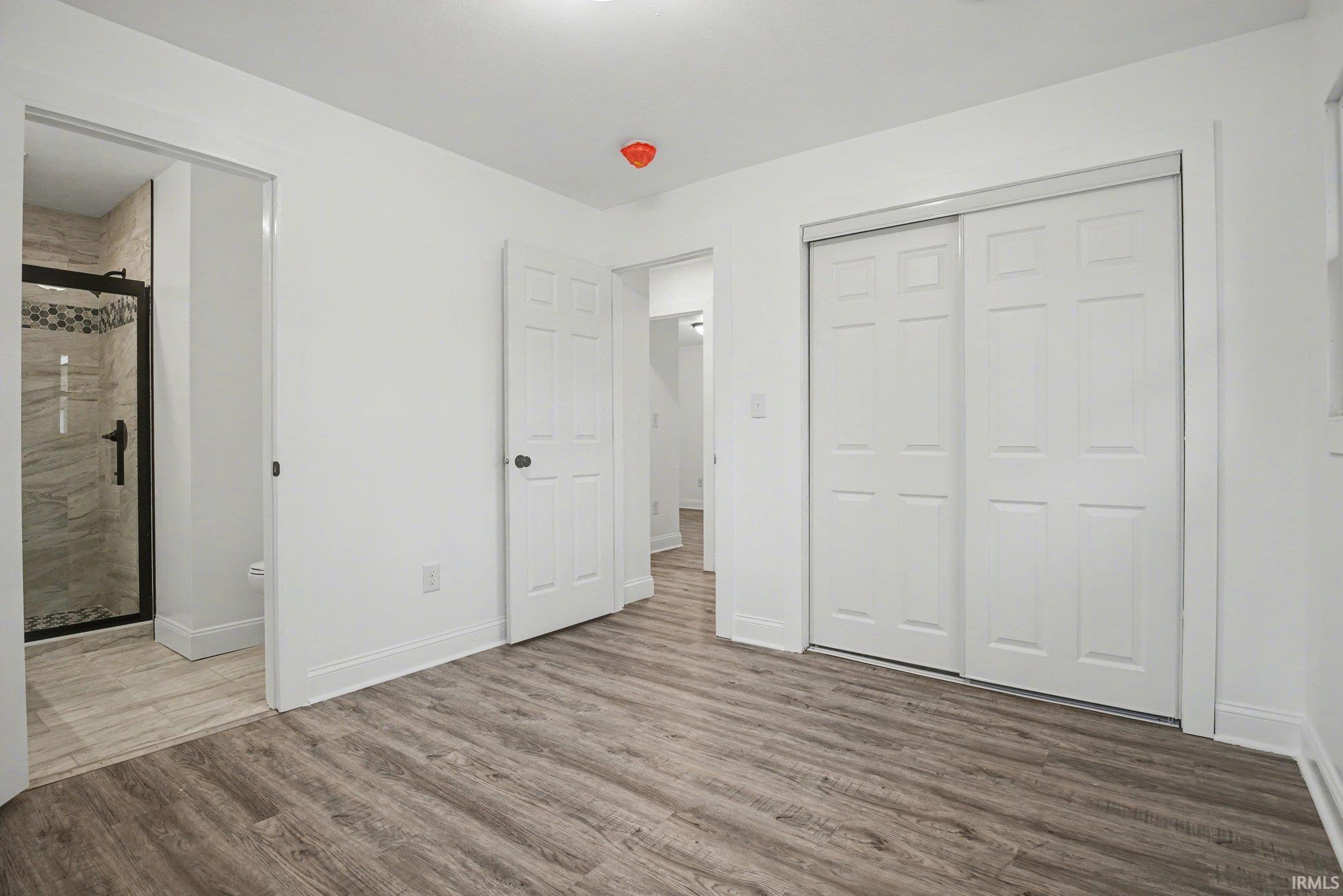Unfurnished bedroom with wood finished floors, ensuite bath, and a closet