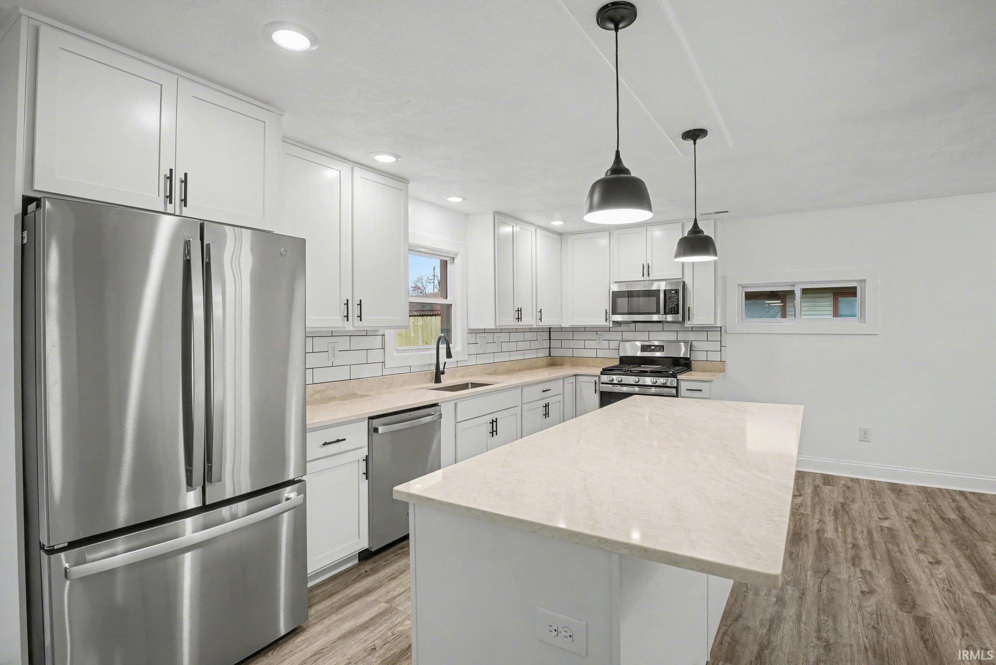 Kitchen featuring stainless steel appliances, white cabinetry, light wood finished floors, decorative backsplash, and a kitchen island