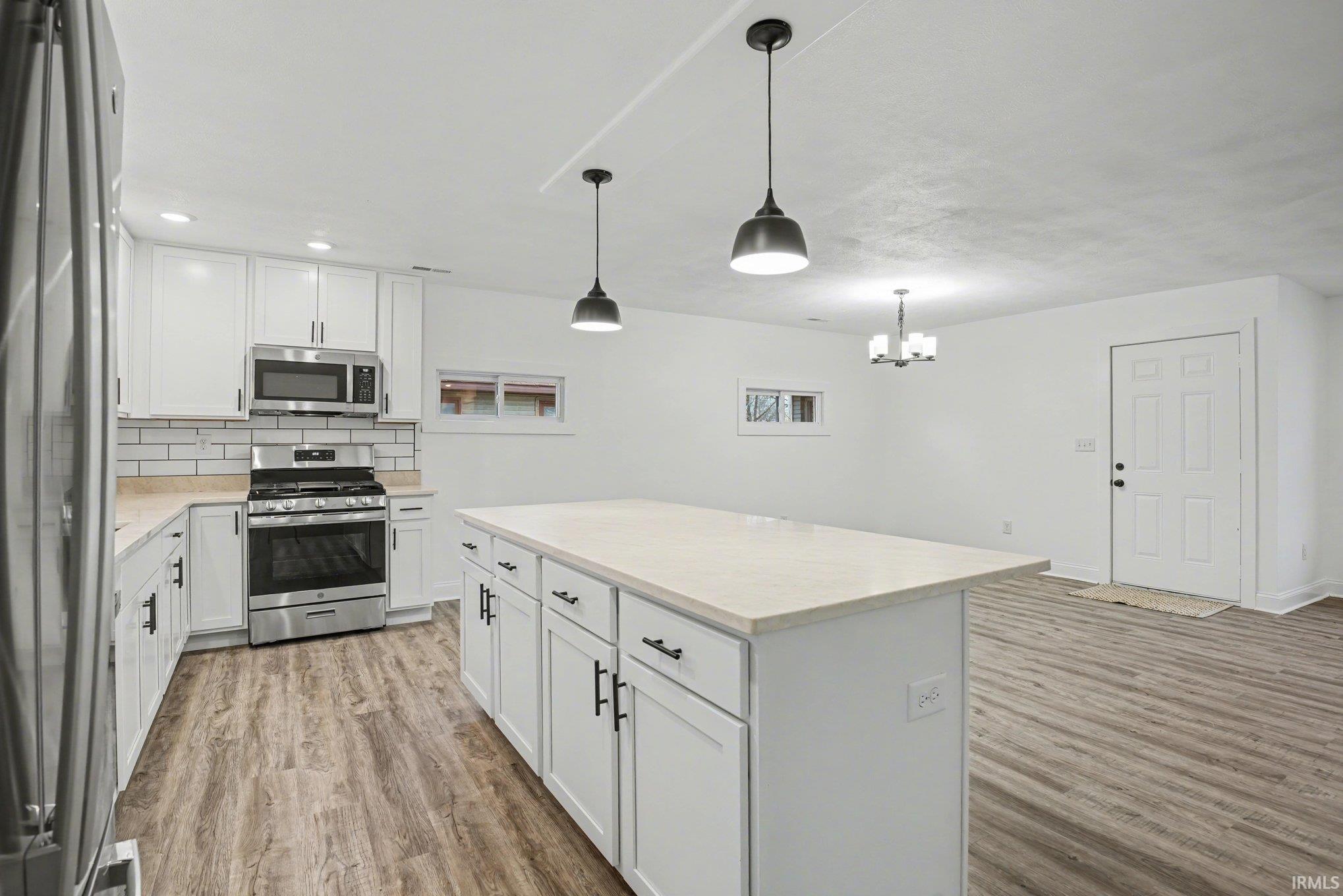 Kitchen with stainless steel appliances, white cabinets, light wood-style floors, and a center island