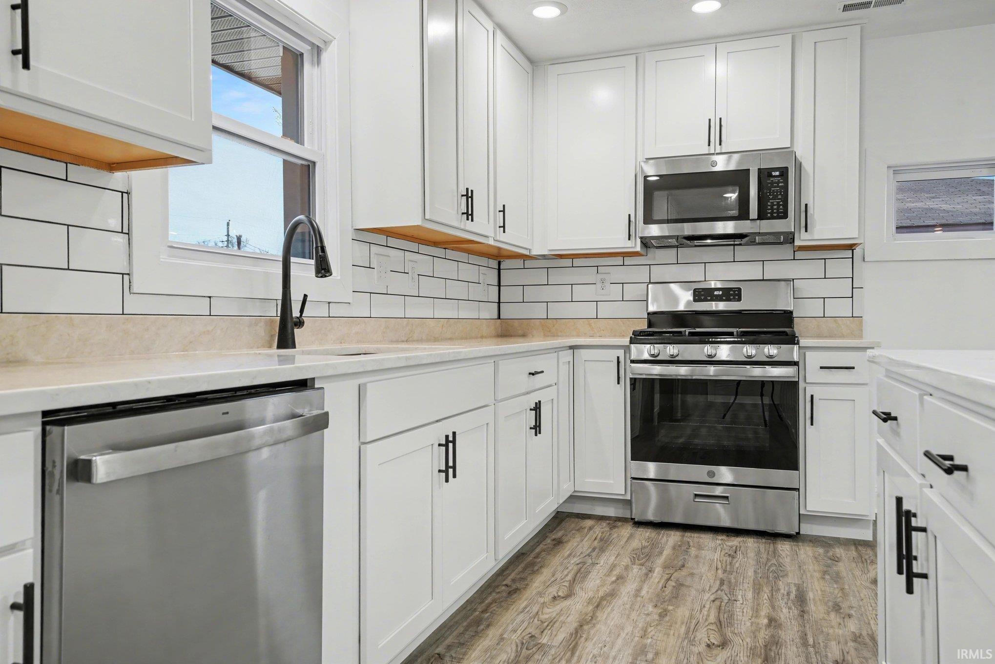 Kitchen with white cabinetry, stainless steel appliances, light wood-style floors, light stone counters, and tasteful backsplash