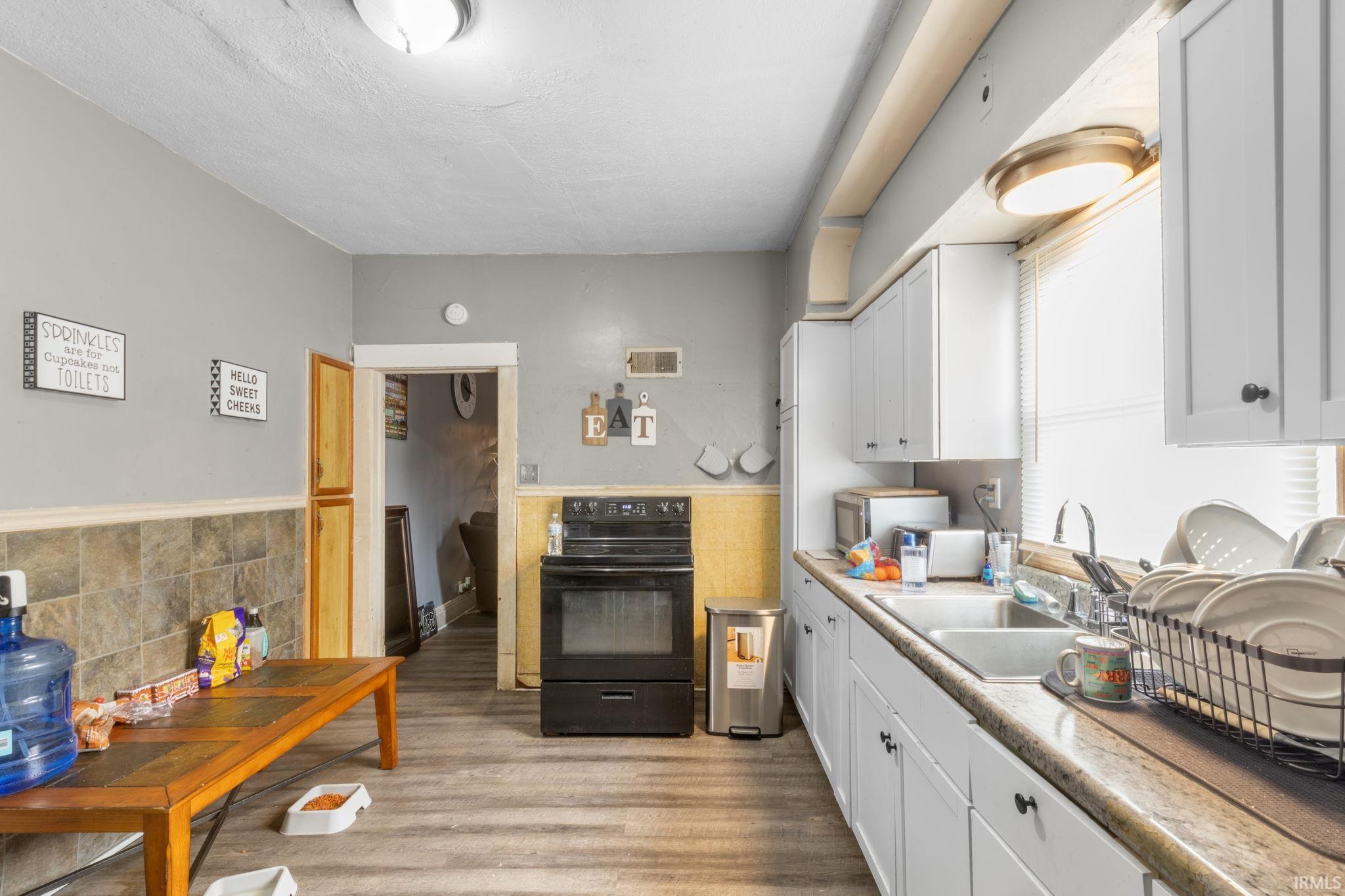Kitchen with white cabinetry, black range with electric cooktop, light countertops, light wood-type flooring, and stainless steel microwave