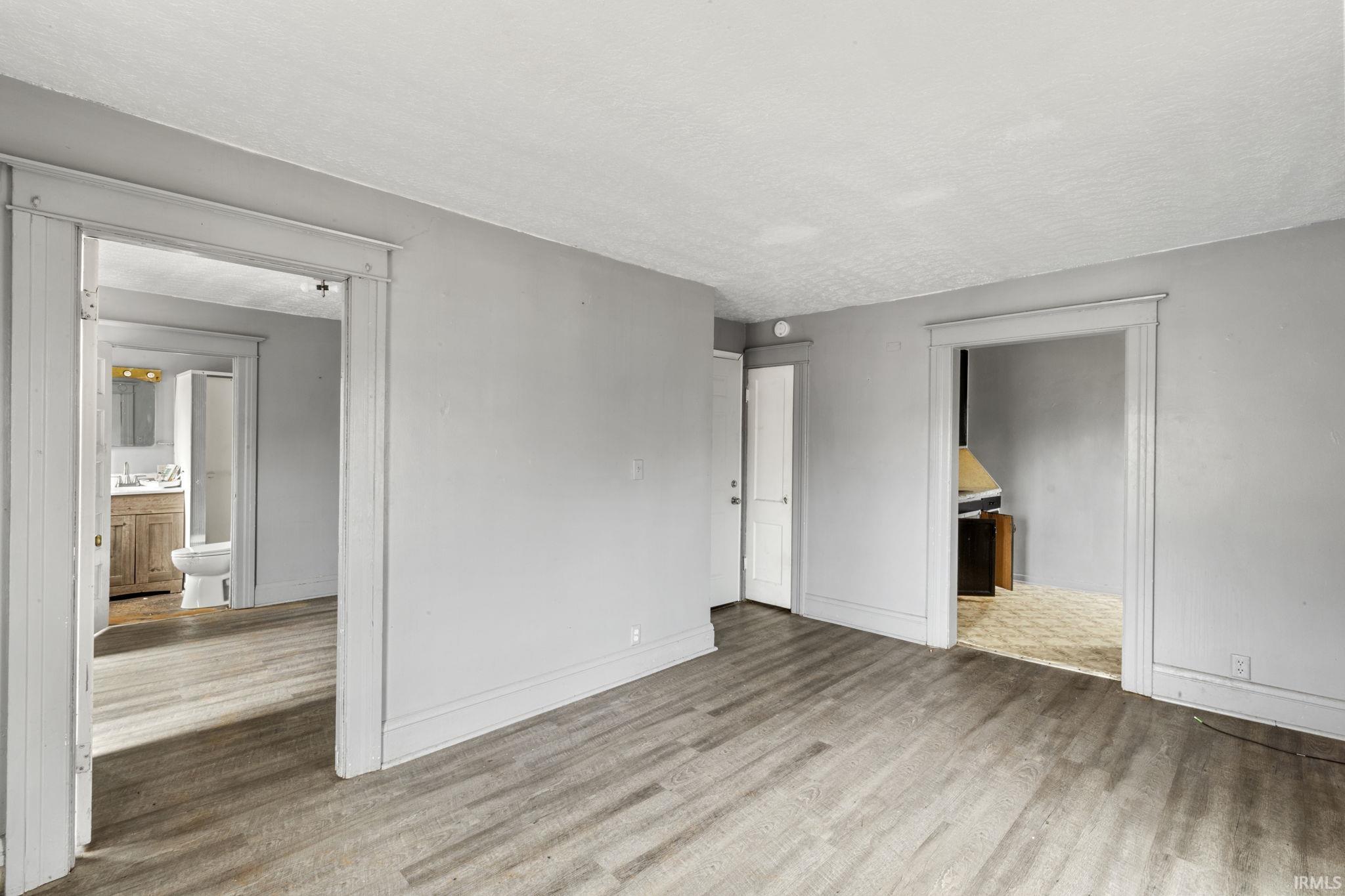 Unfurnished bedroom with ensuite bathroom, light wood-type flooring, and a textured ceiling