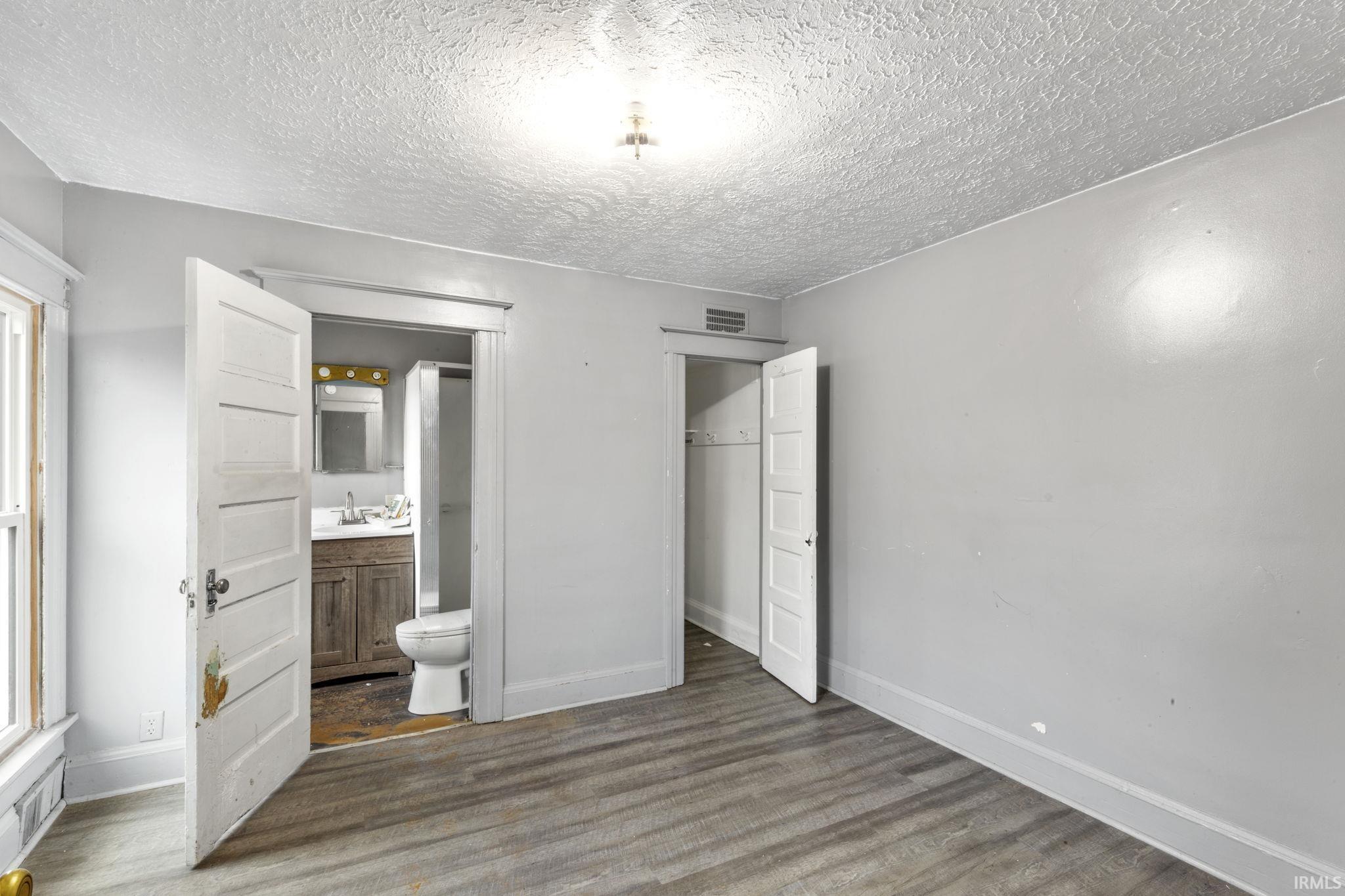 Unfurnished bedroom with a textured ceiling, dark wood-type flooring, and connected bathroom