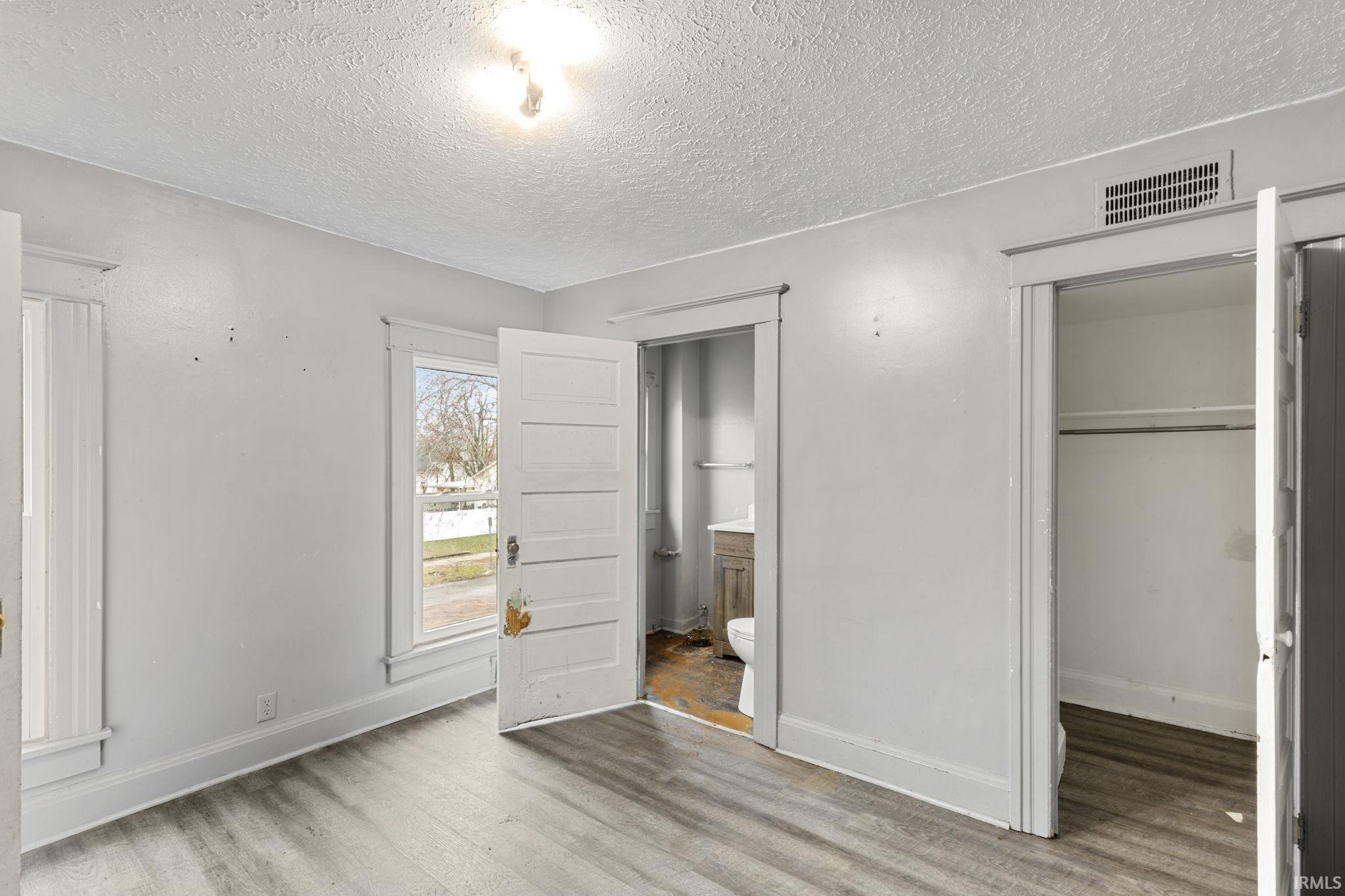 Unfurnished bedroom featuring a textured ceiling, light wood-style floors, ensuite bathroom, and a walk in closet