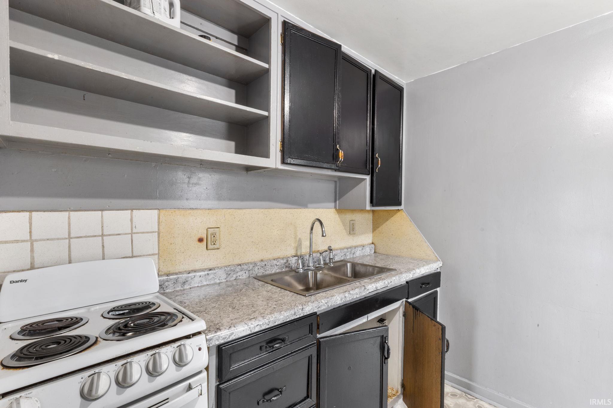 Kitchen with white range with electric stovetop, light countertops, backsplash, open shelves, and dark cabinetry