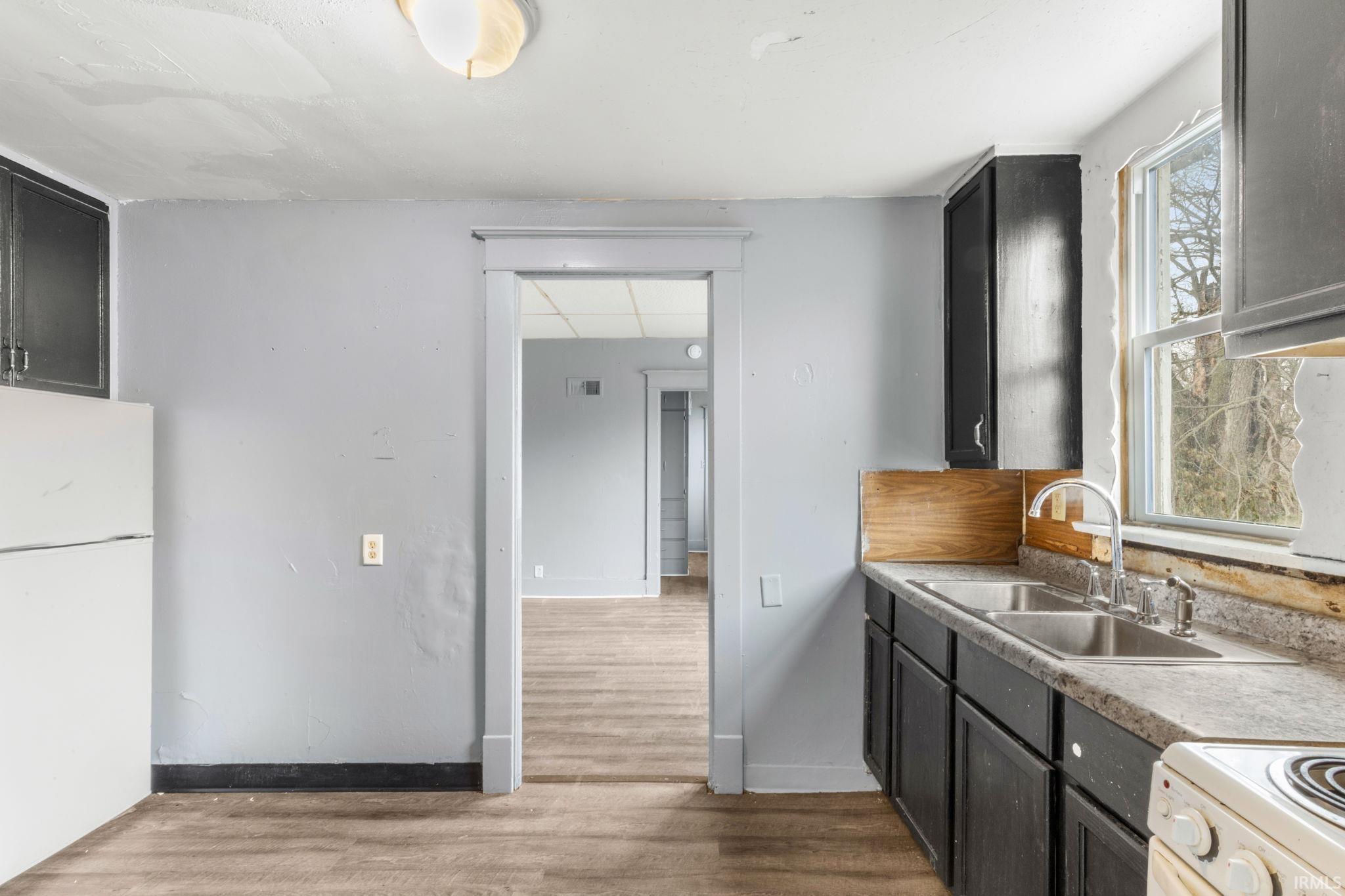 Kitchen featuring freestanding refrigerator, light wood-type flooring, light countertops, and dark cabinetry