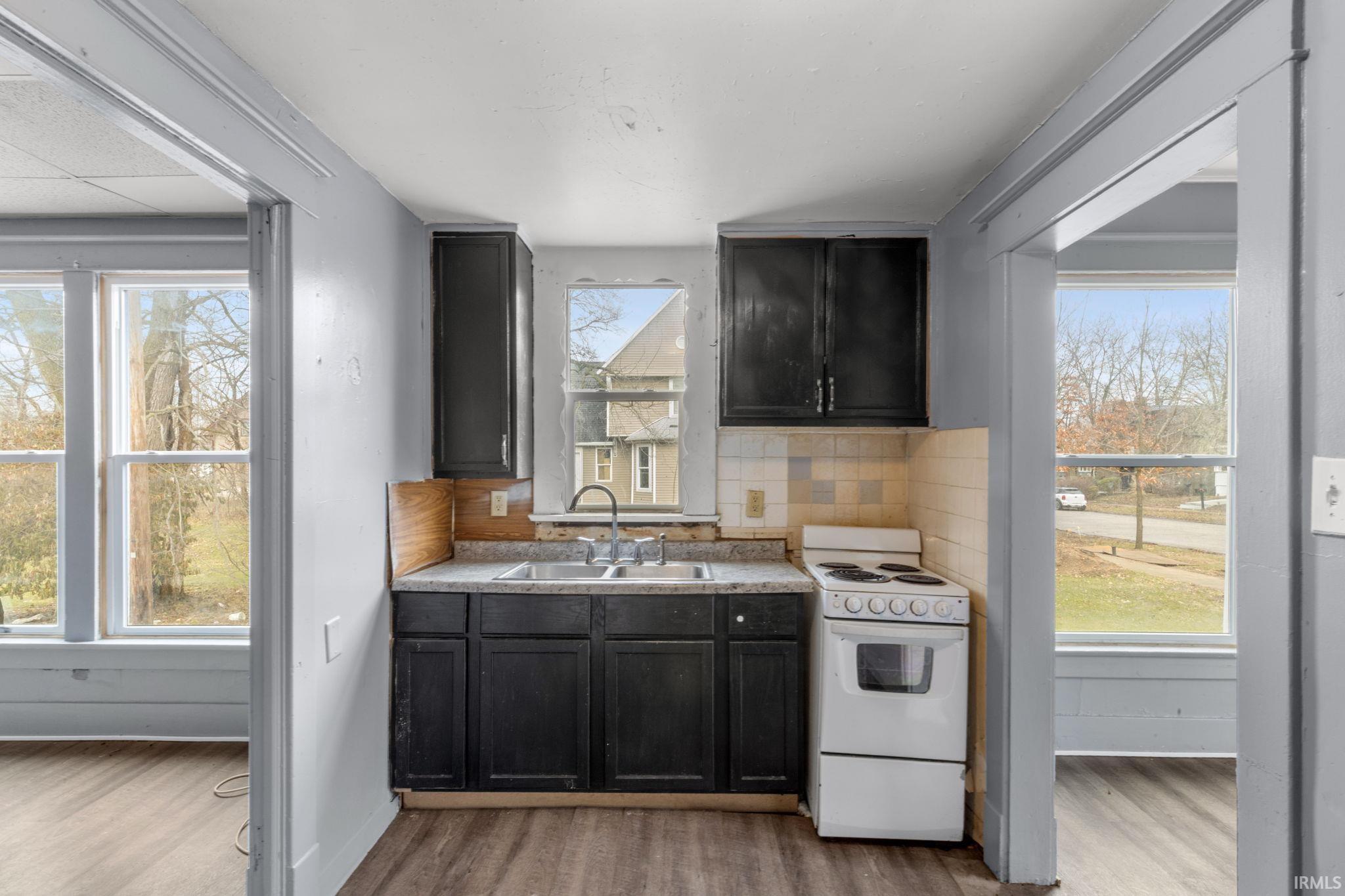 Kitchen featuring electric range, light wood finished floors, dark cabinetry, tasteful backsplash, and light countertops
