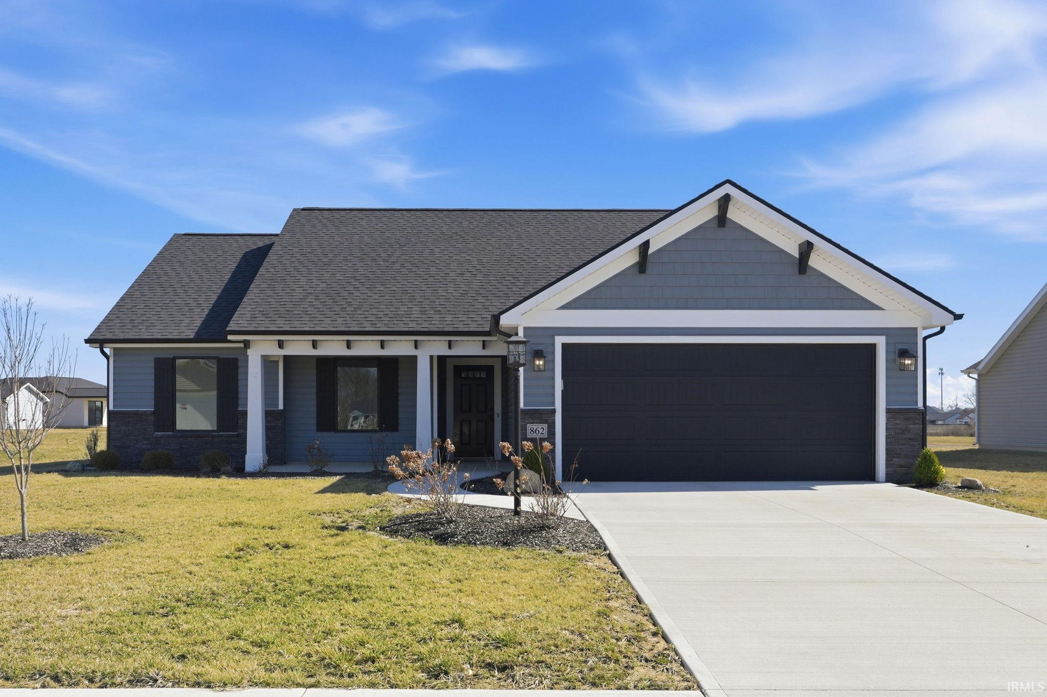 View of front of property featuring stone siding, a garage, a front yard, driveway, and covered porch