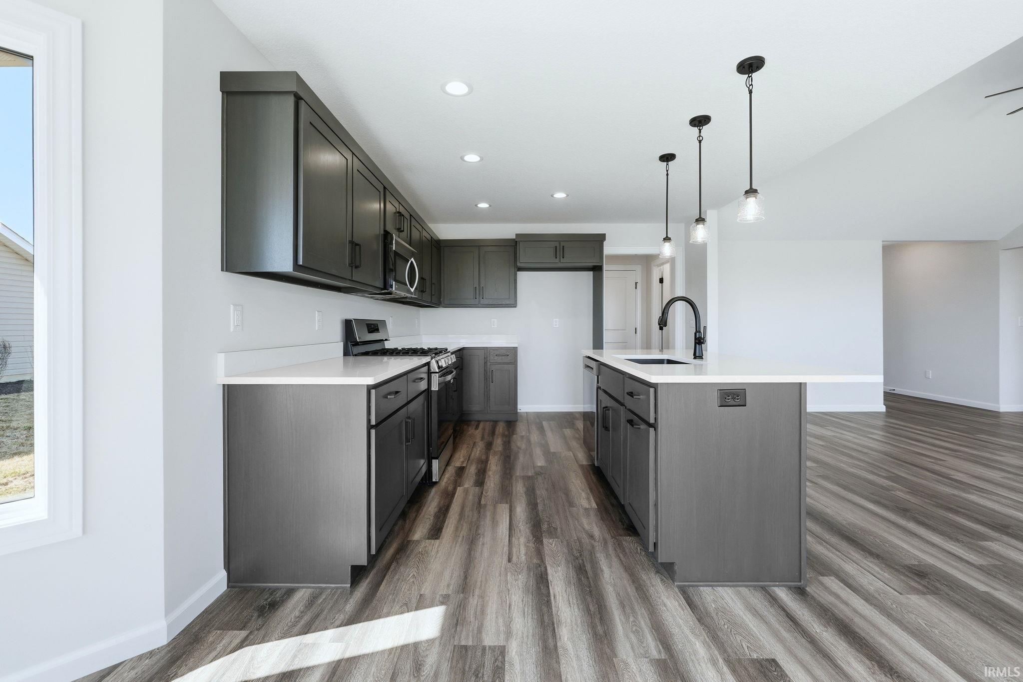 Kitchen featuring stainless steel appliances, pendant lighting, dark wood-style floors, a center island with sink, and light stone counters