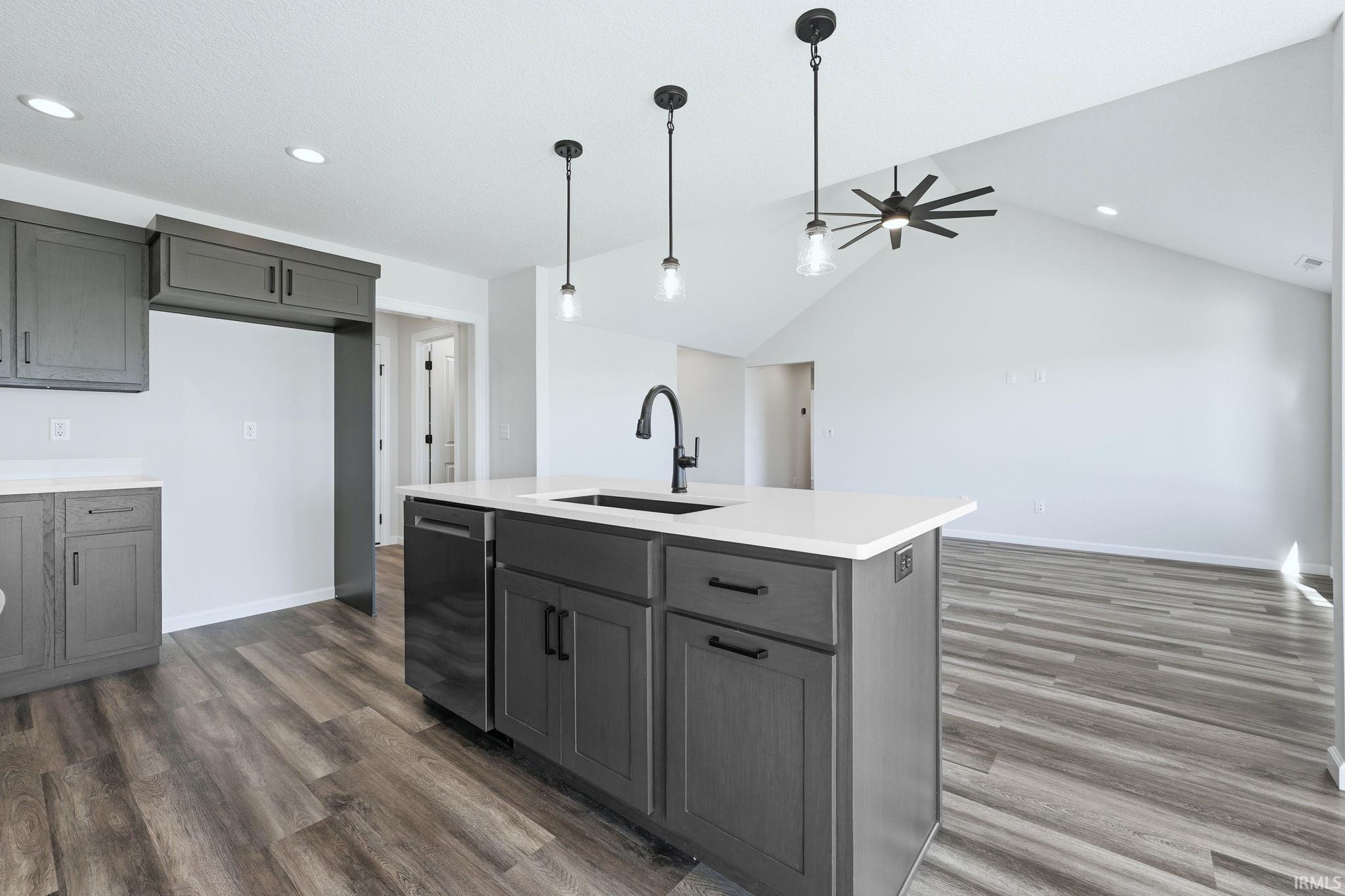 Kitchen with gray cabinets, decorative light fixtures, stainless steel dishwasher, dark wood finished floors, and lofted ceiling