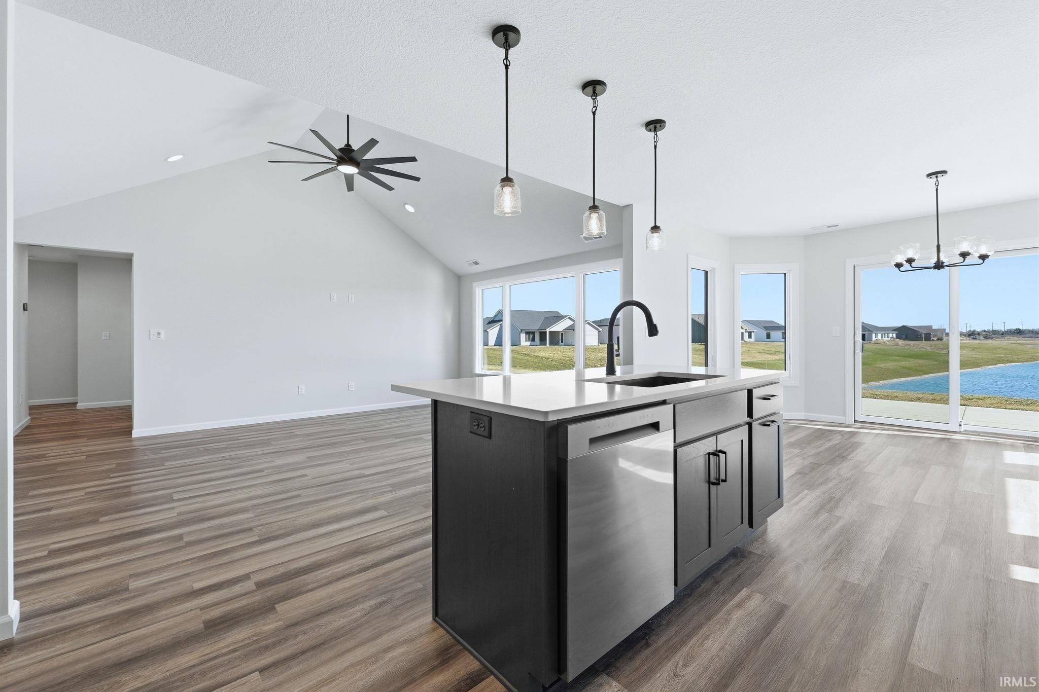 Kitchen featuring a high ceiling, a center island with sink, stainless steel dishwasher, open floor plan, and hanging lights