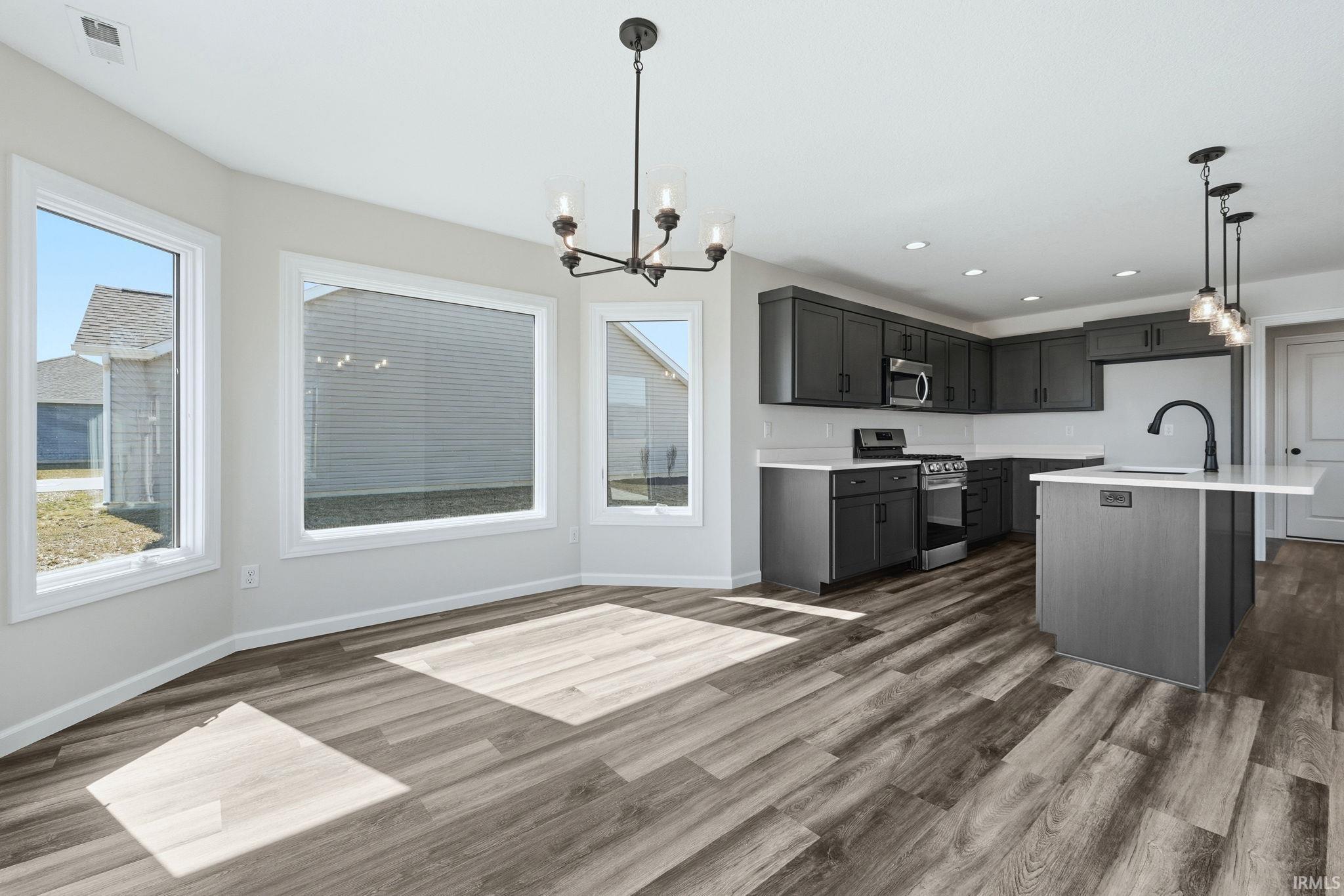 Kitchen featuring hanging lights, stainless steel appliances, dark wood-style floors, and an island with sink