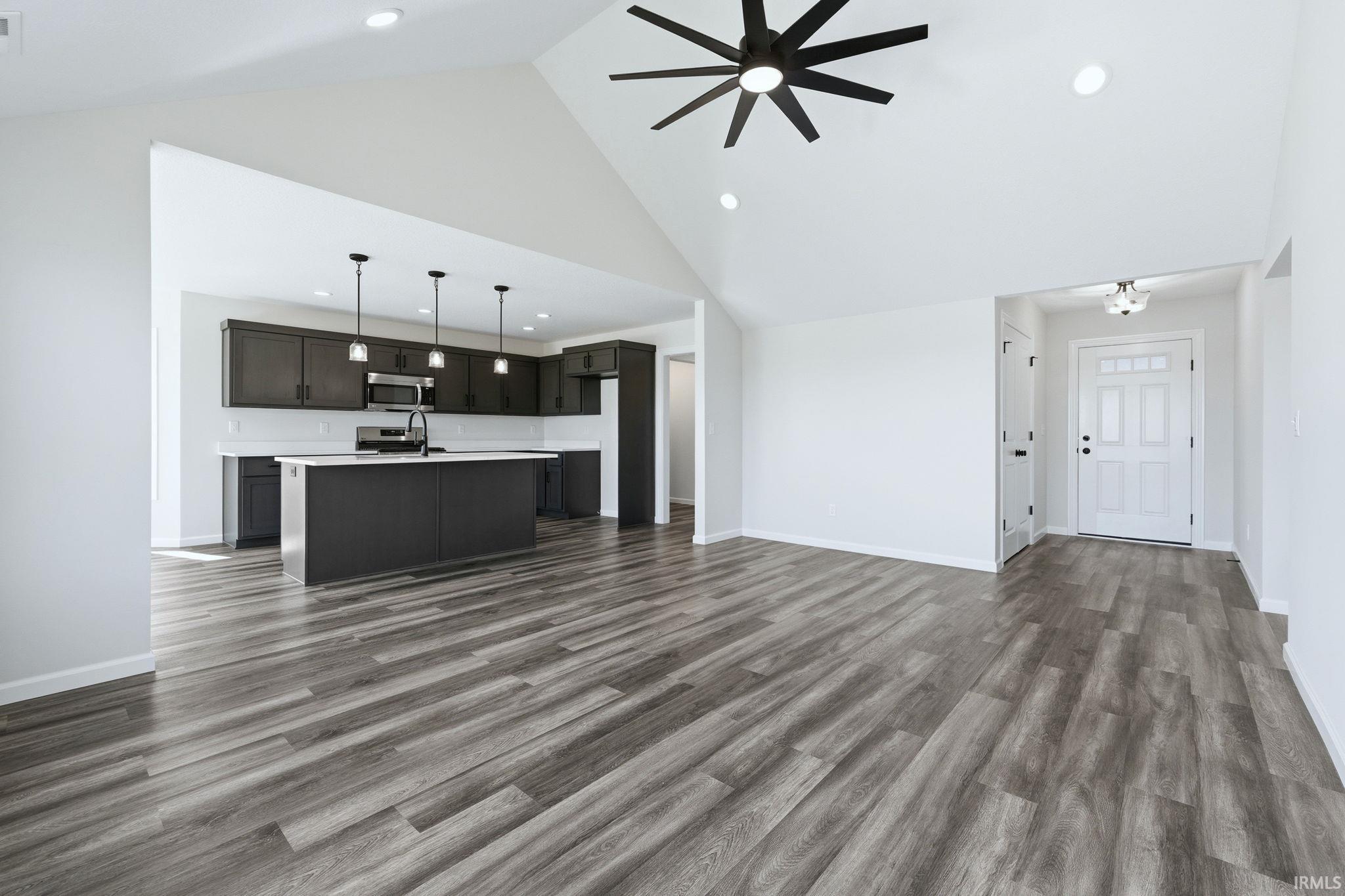Unfurnished living room featuring dark wood-style flooring, ceiling fan, lofted ceiling, and recessed lighting