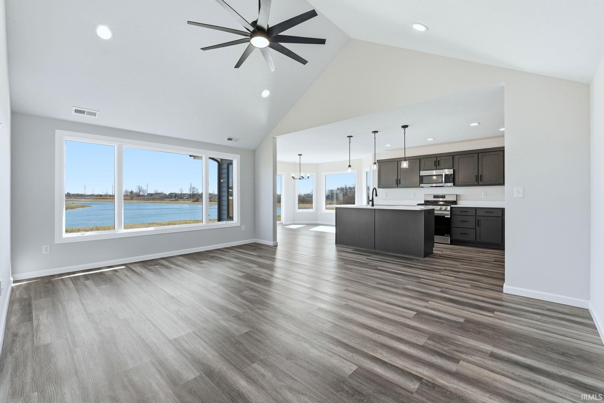 Unfurnished living room featuring ceiling fan, dark wood-style flooring, a high ceiling, and suspended lighting