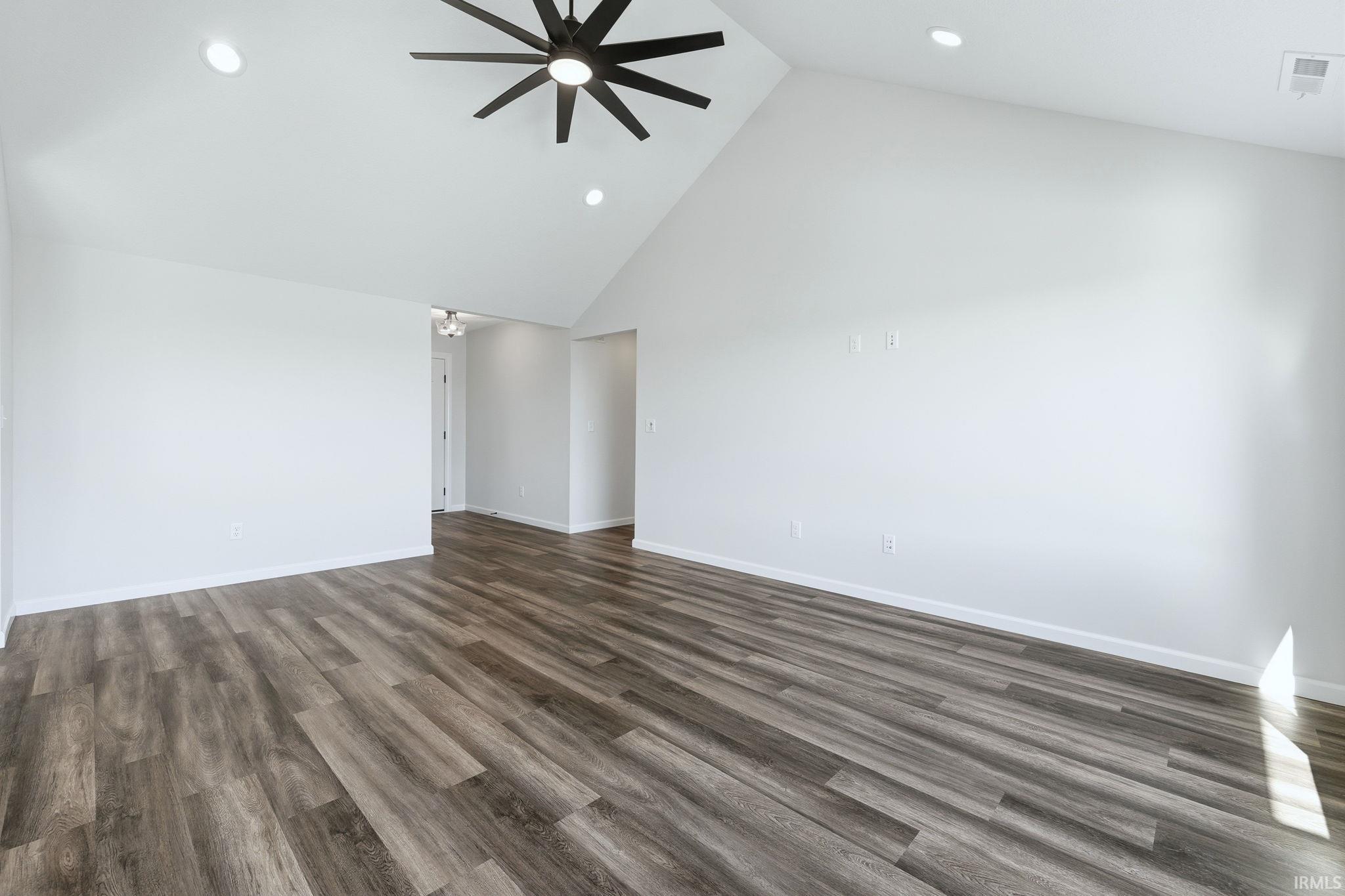 Empty room featuring a high ceiling, a ceiling fan, dark wood finished floors, and recessed lighting
