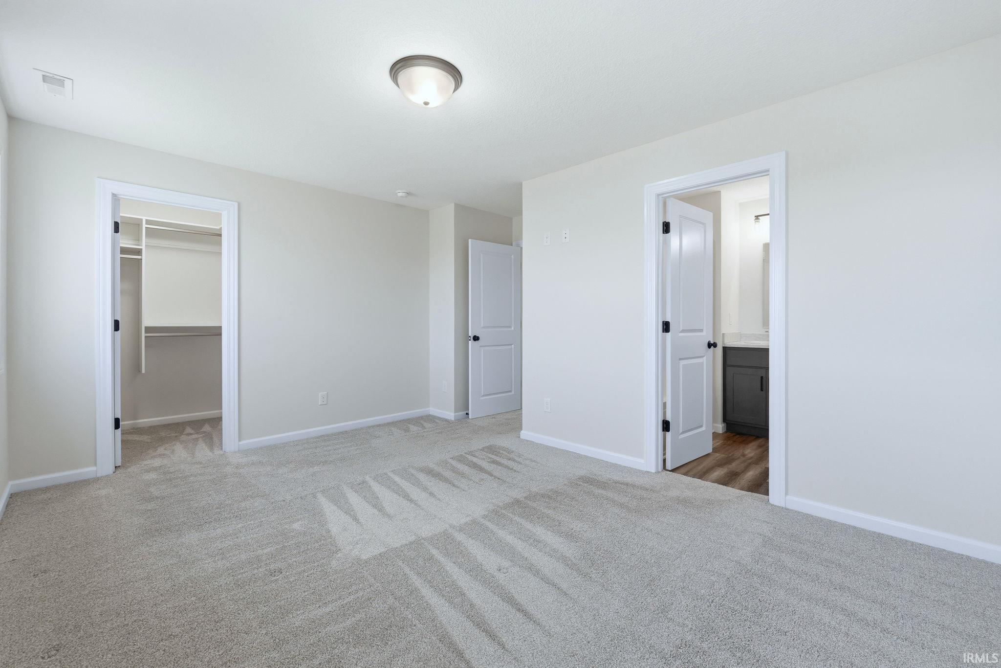Unfurnished bedroom with a spacious closet, light carpet, and ensuite bathroom