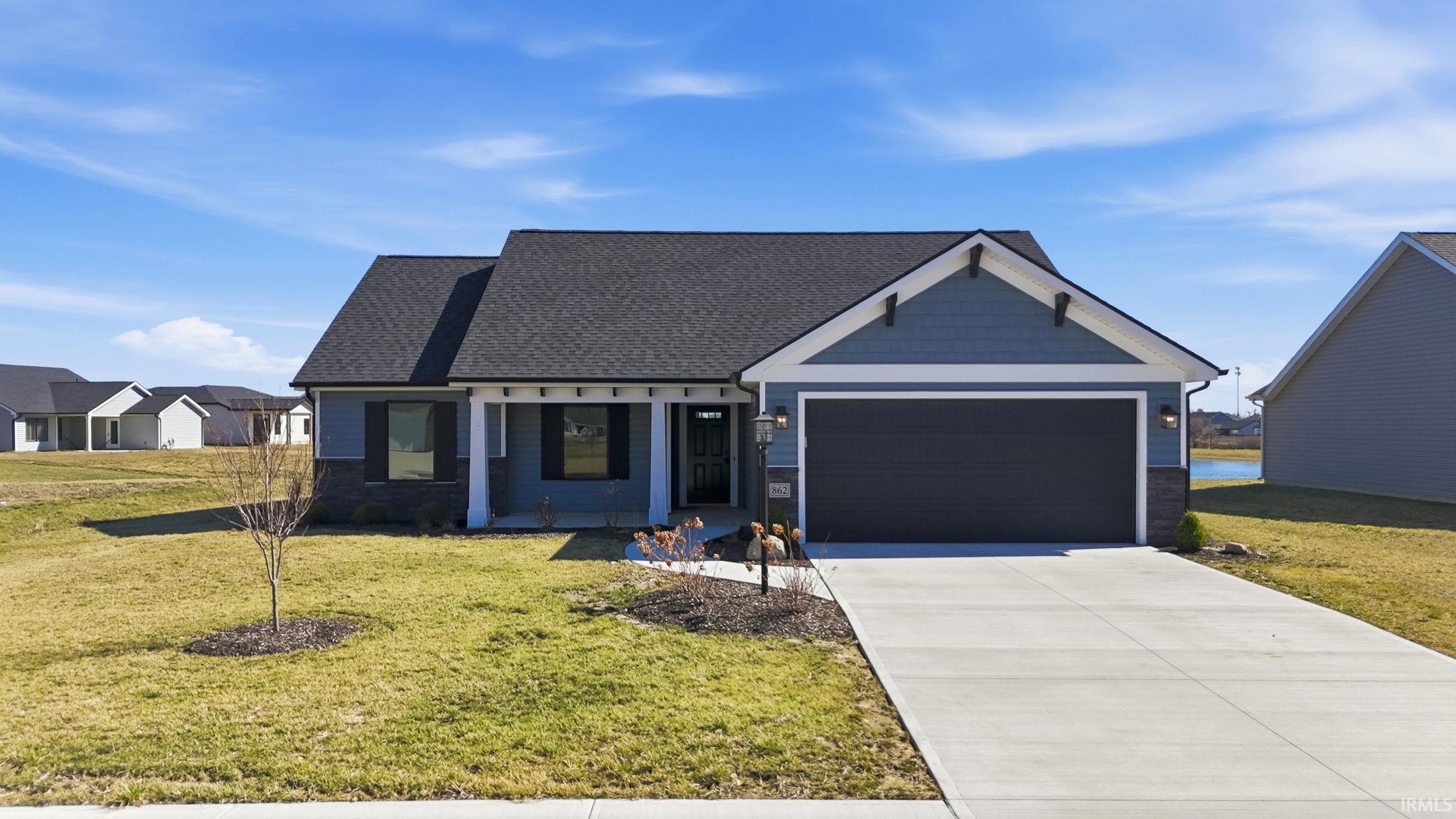 View of front of house with a front lawn, an attached garage, driveway, covered porch, and stone siding
