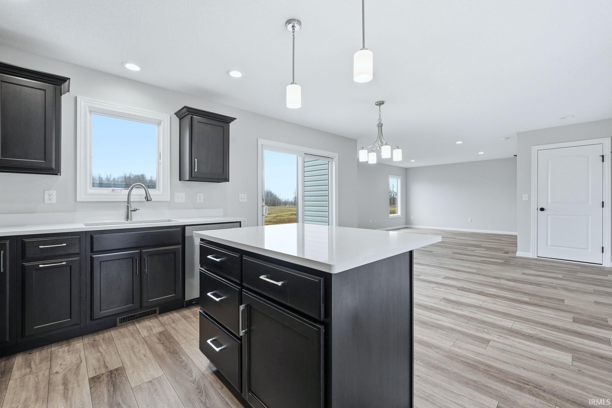 Kitchen with light wood finished floors, hanging light fixtures, a center island, and plenty of natural light