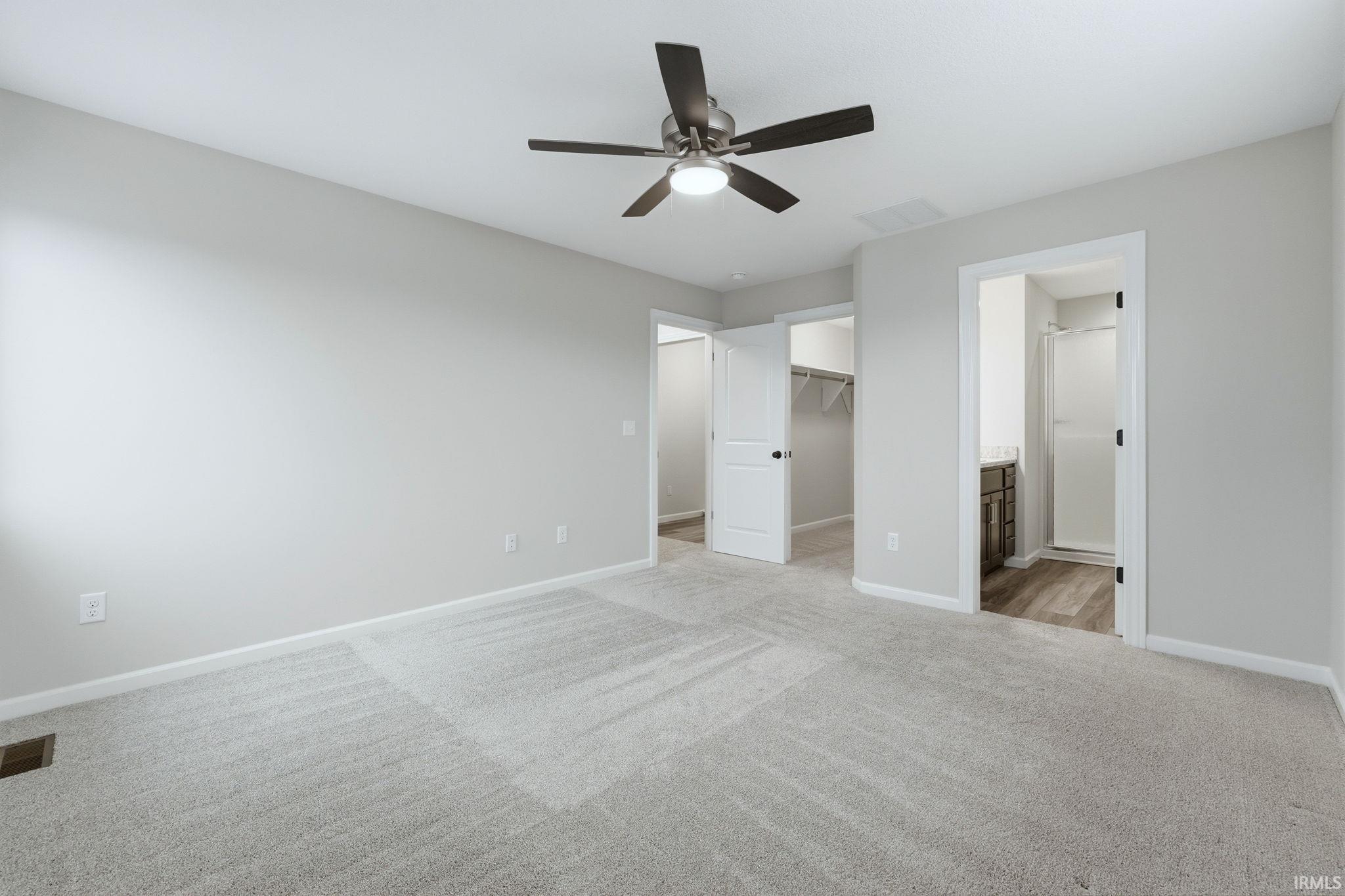 Unfurnished bedroom with light carpet, a spacious closet, a ceiling fan, and ensuite bath