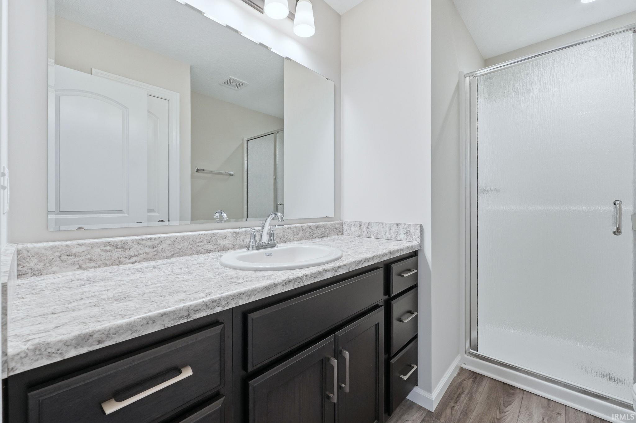 Full bath featuring a stall shower, vanity, and light wood-style floors