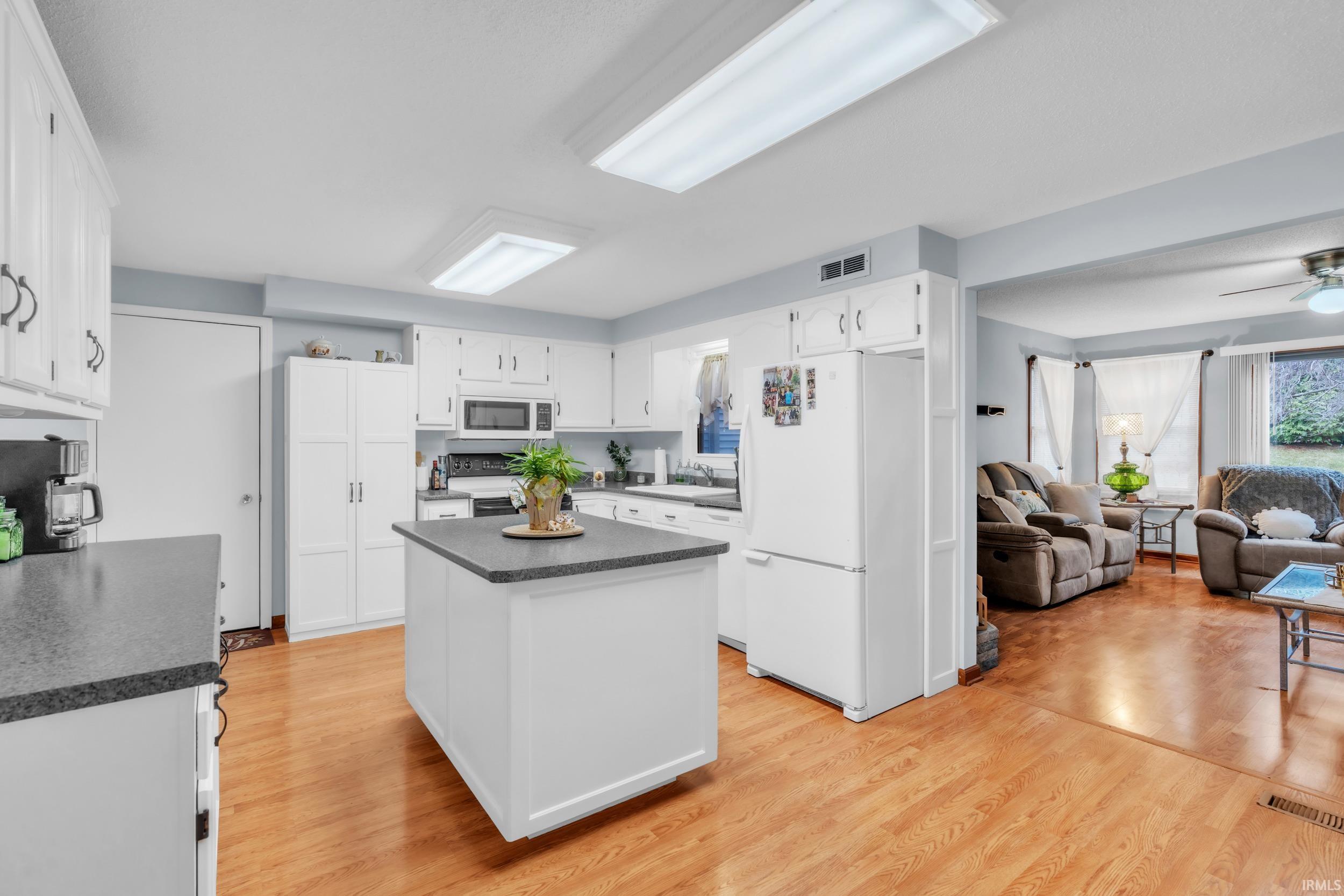 Kitchen featuring dark countertops, white appliances, open floor plan, and white cabinetry