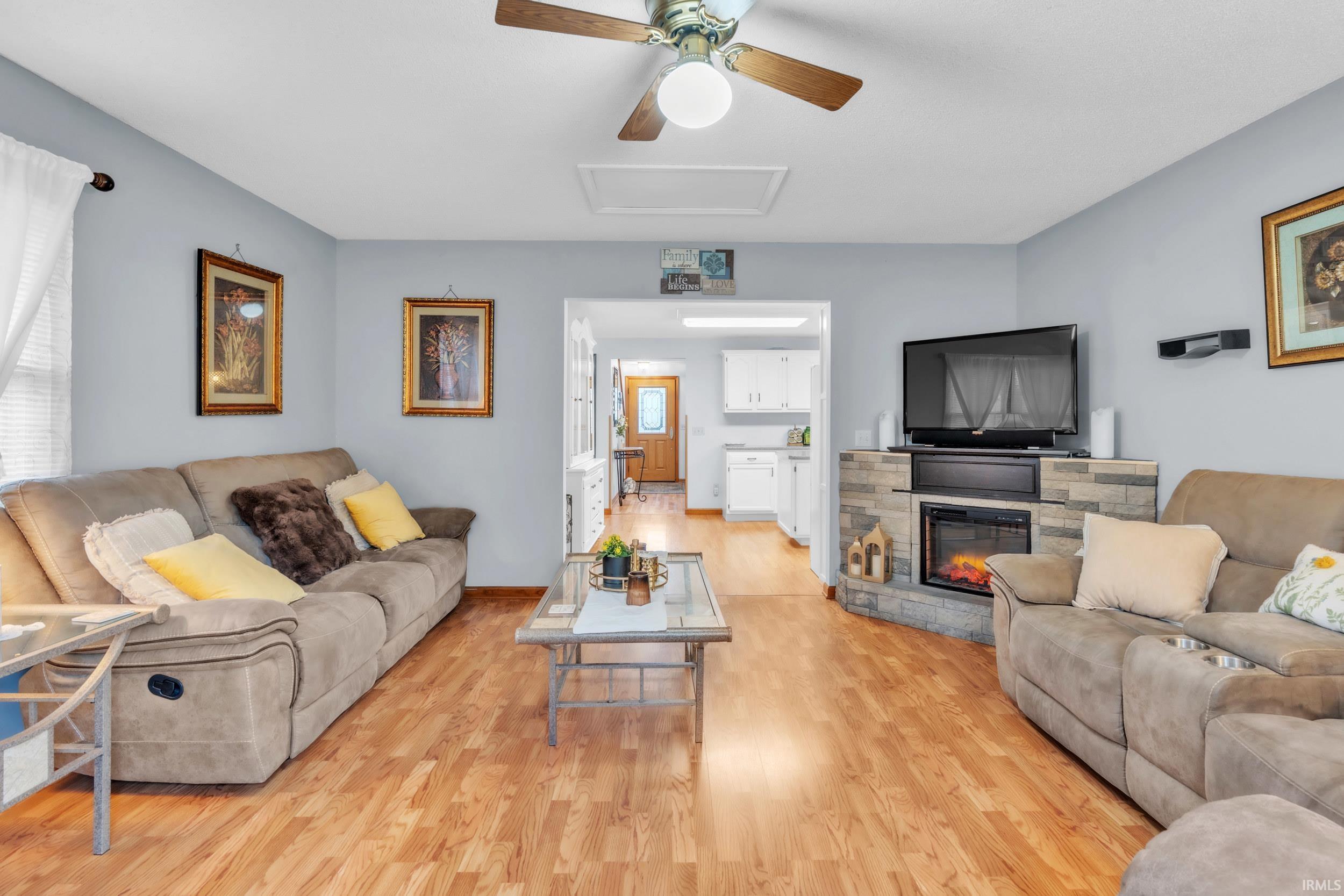 Living area featuring light wood-type flooring, ceiling fan, and a stone fireplace