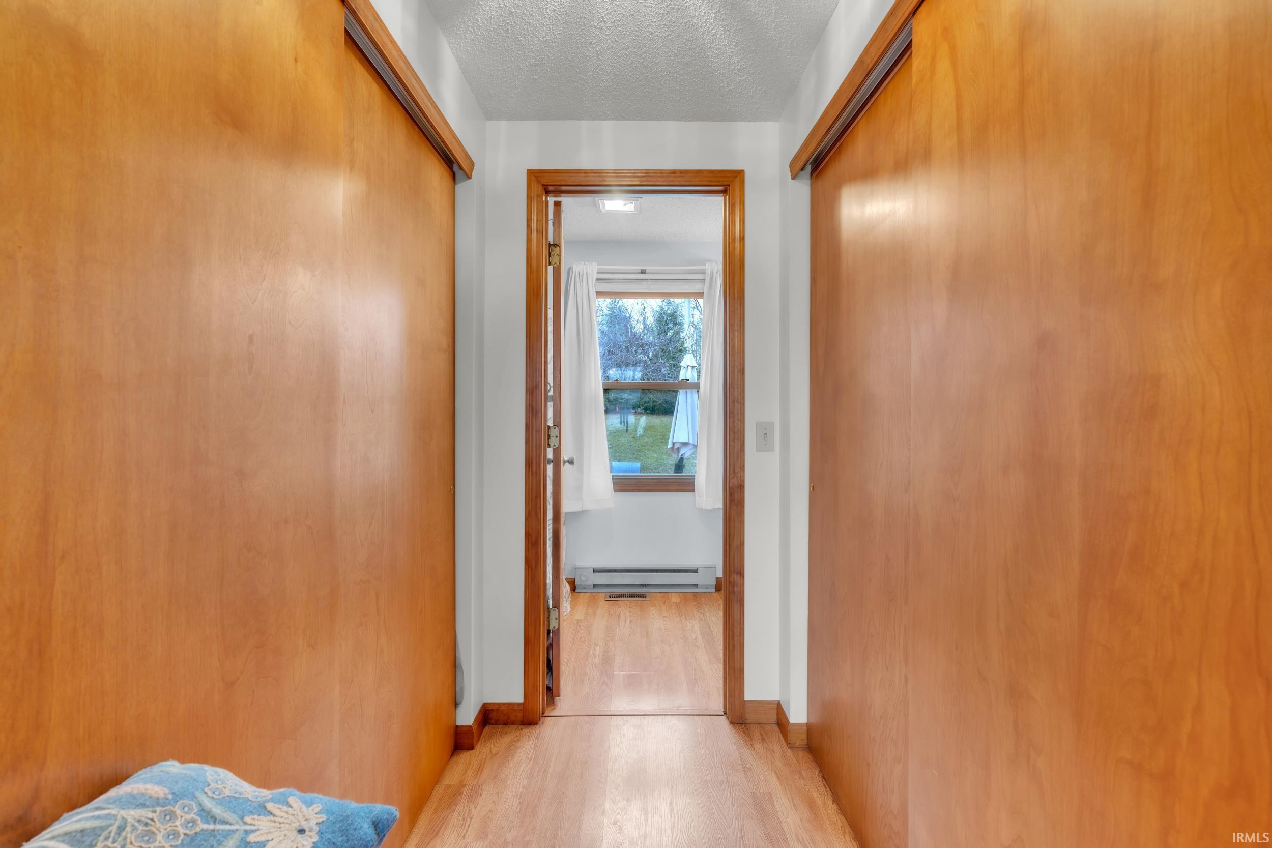 Hall featuring a textured ceiling, light wood-type flooring, and a baseboard radiator