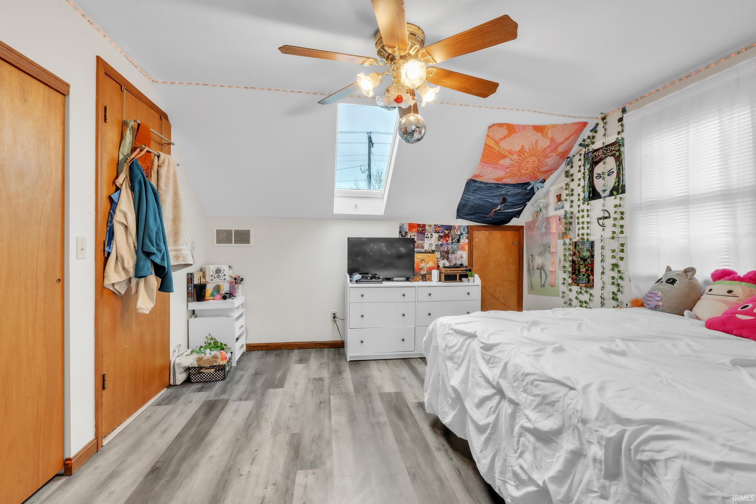 Bedroom with a skylight, light wood-type flooring, ceiling fan, and vaulted ceiling