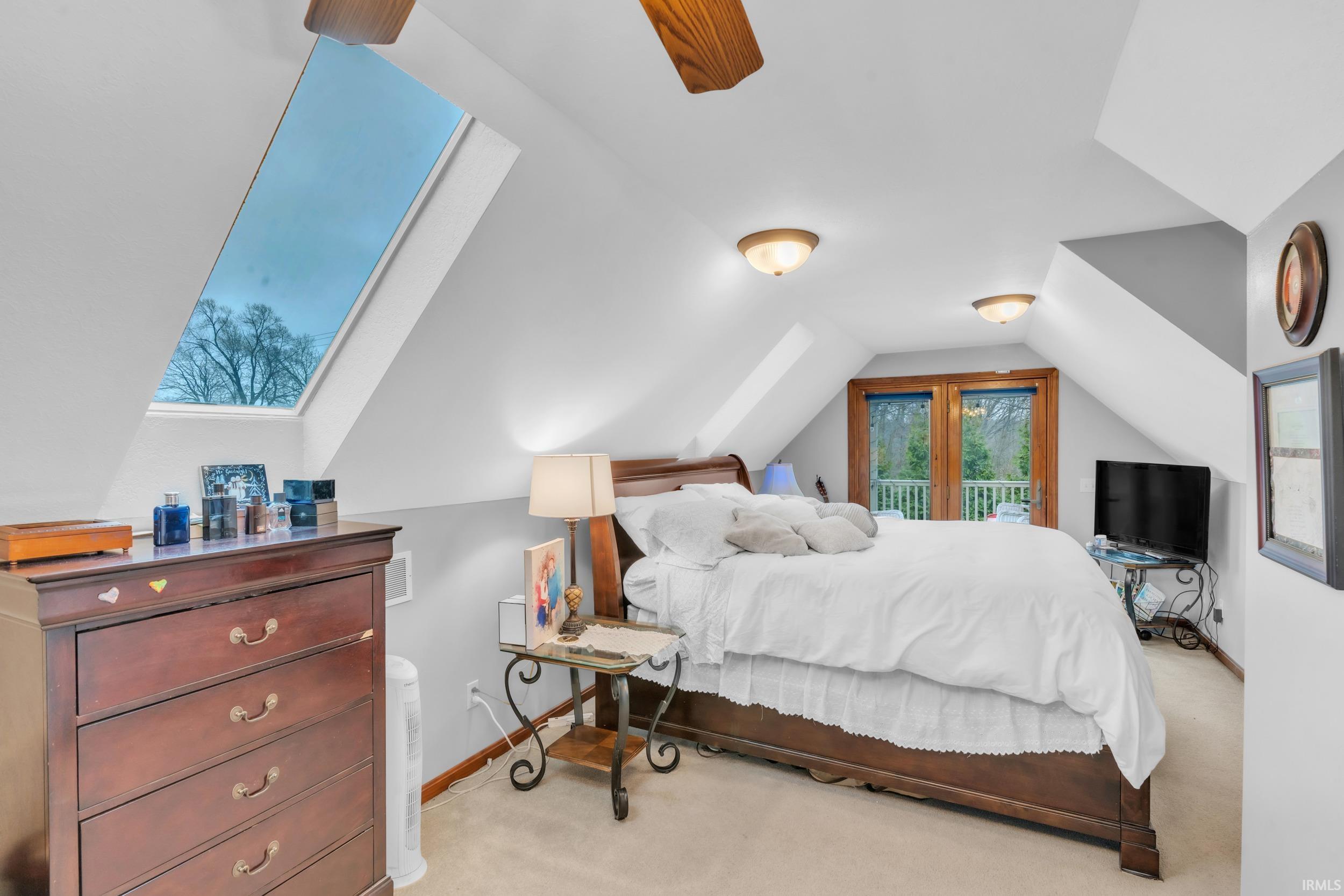 Bedroom with vaulted ceiling, light colored carpet, and access to exterior