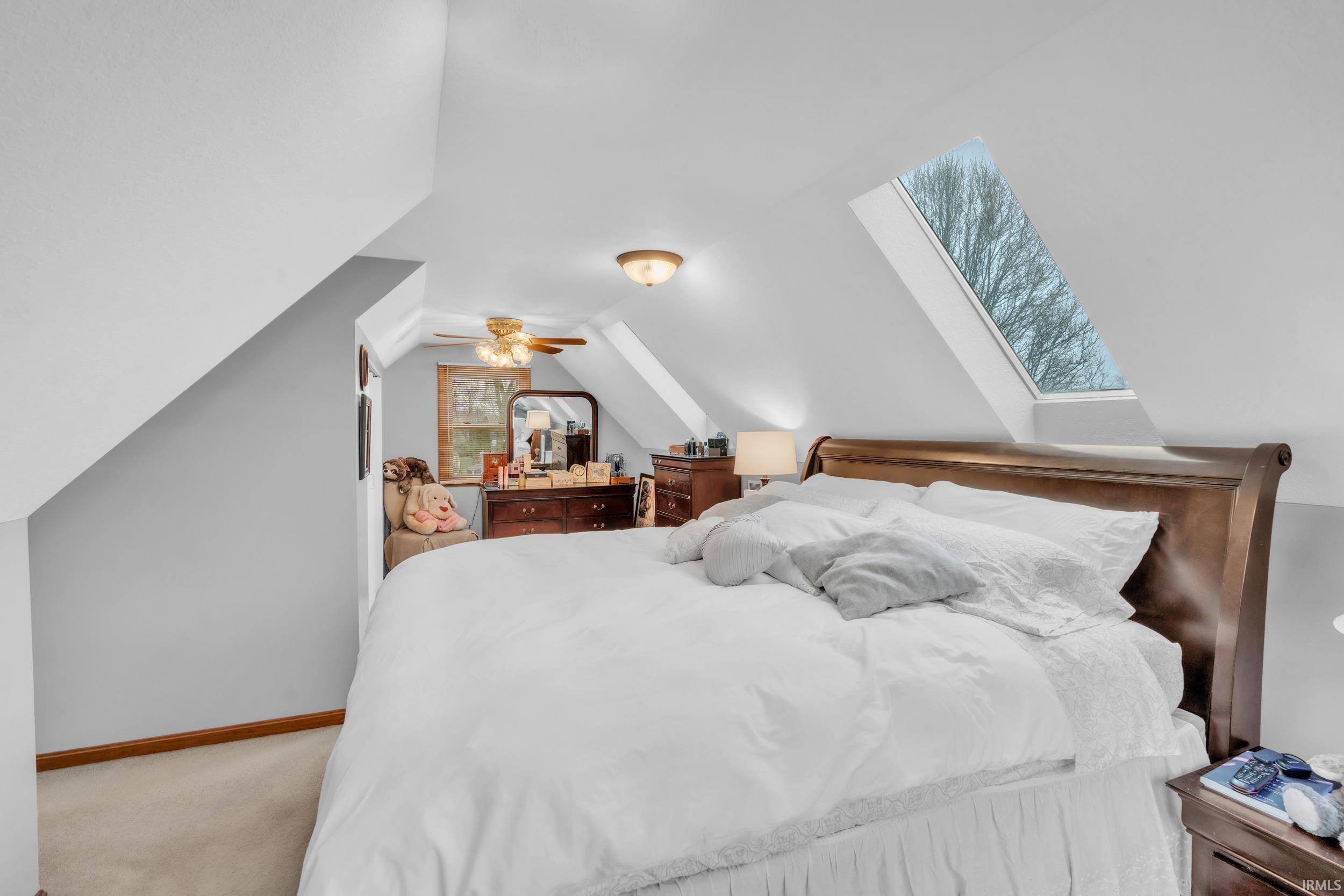 Bedroom featuring a skylight, lofted ceiling, light colored carpet, and ceiling fan