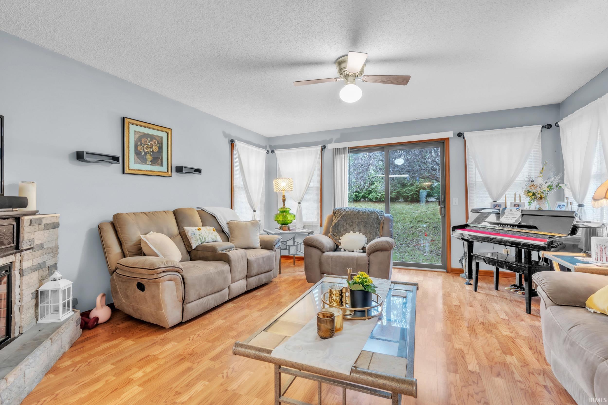Living area featuring a fireplace, light wood-style flooring, a textured ceiling, and a ceiling fan