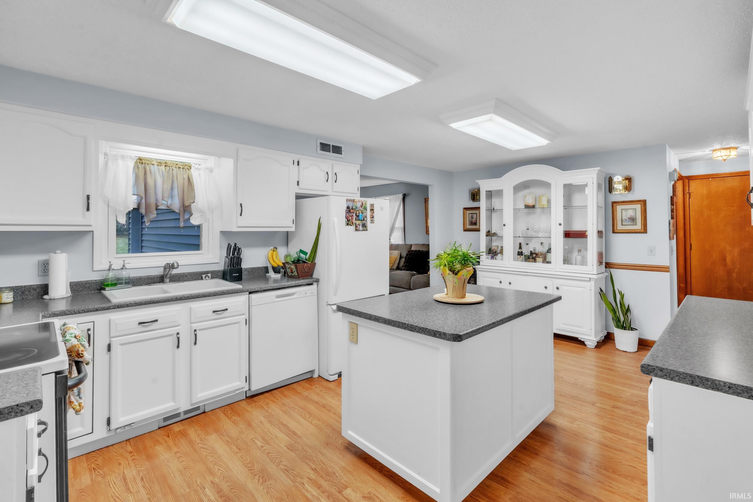 Kitchen with dark countertops, white cabinetry, light wood finished floors, white dishwasher, and electric stove
