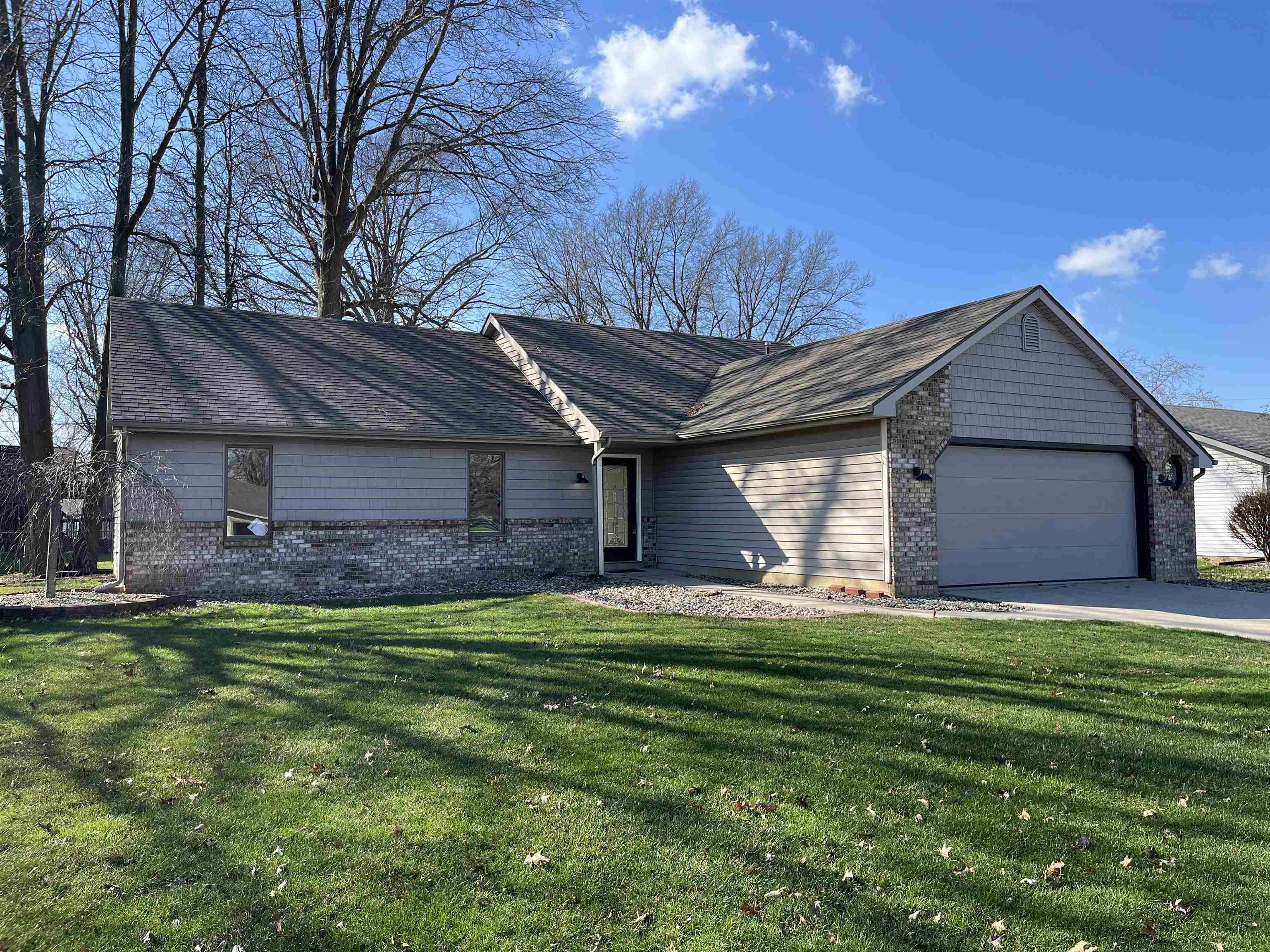 Ranch-style home with an attached garage, a front lawn, brick siding, and driveway
