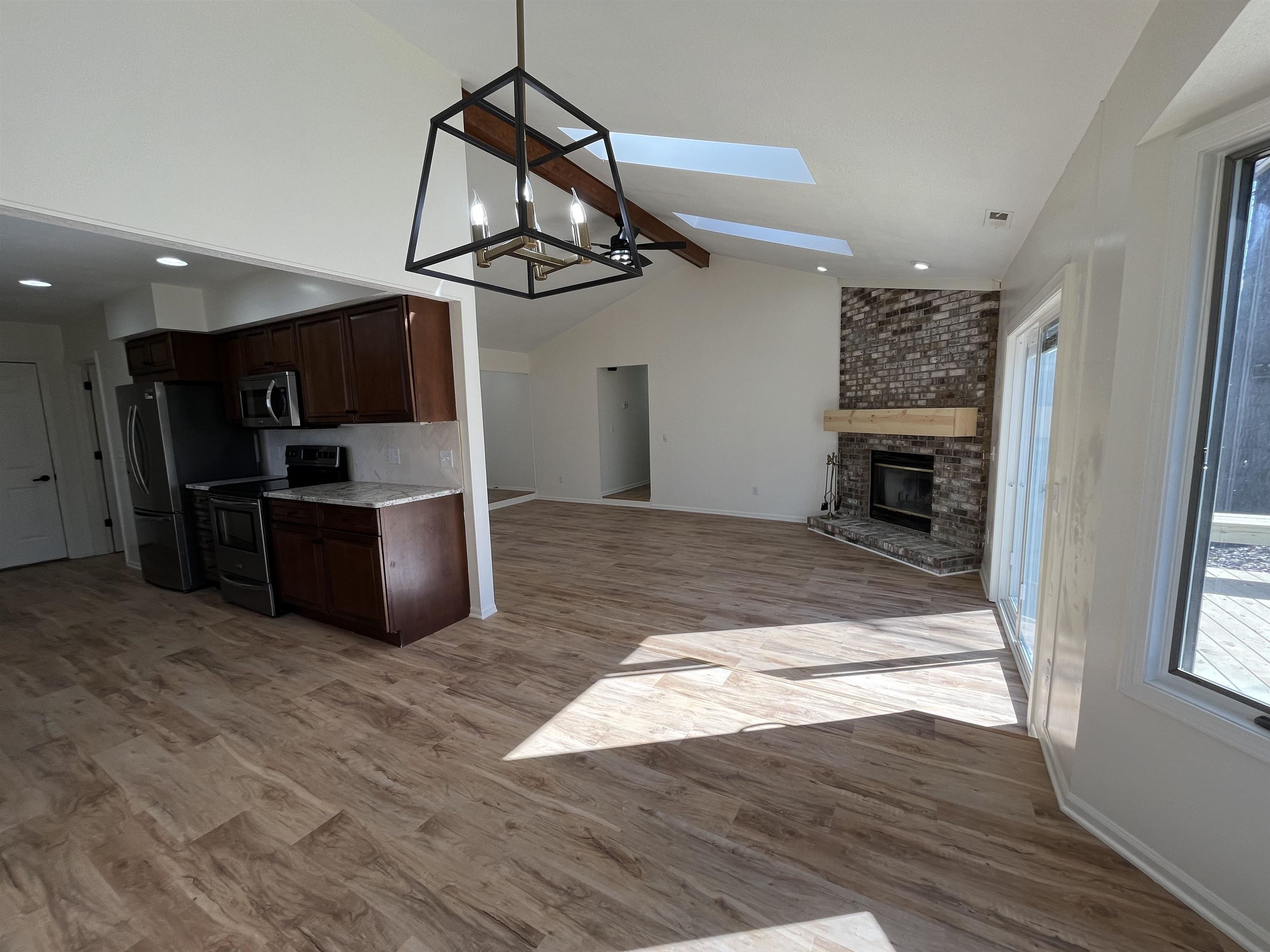 Kitchen with dark wood finish cabinetry, vaulted ceiling with beams, light wood finished floors, stainless steel appliances, and a fireplace