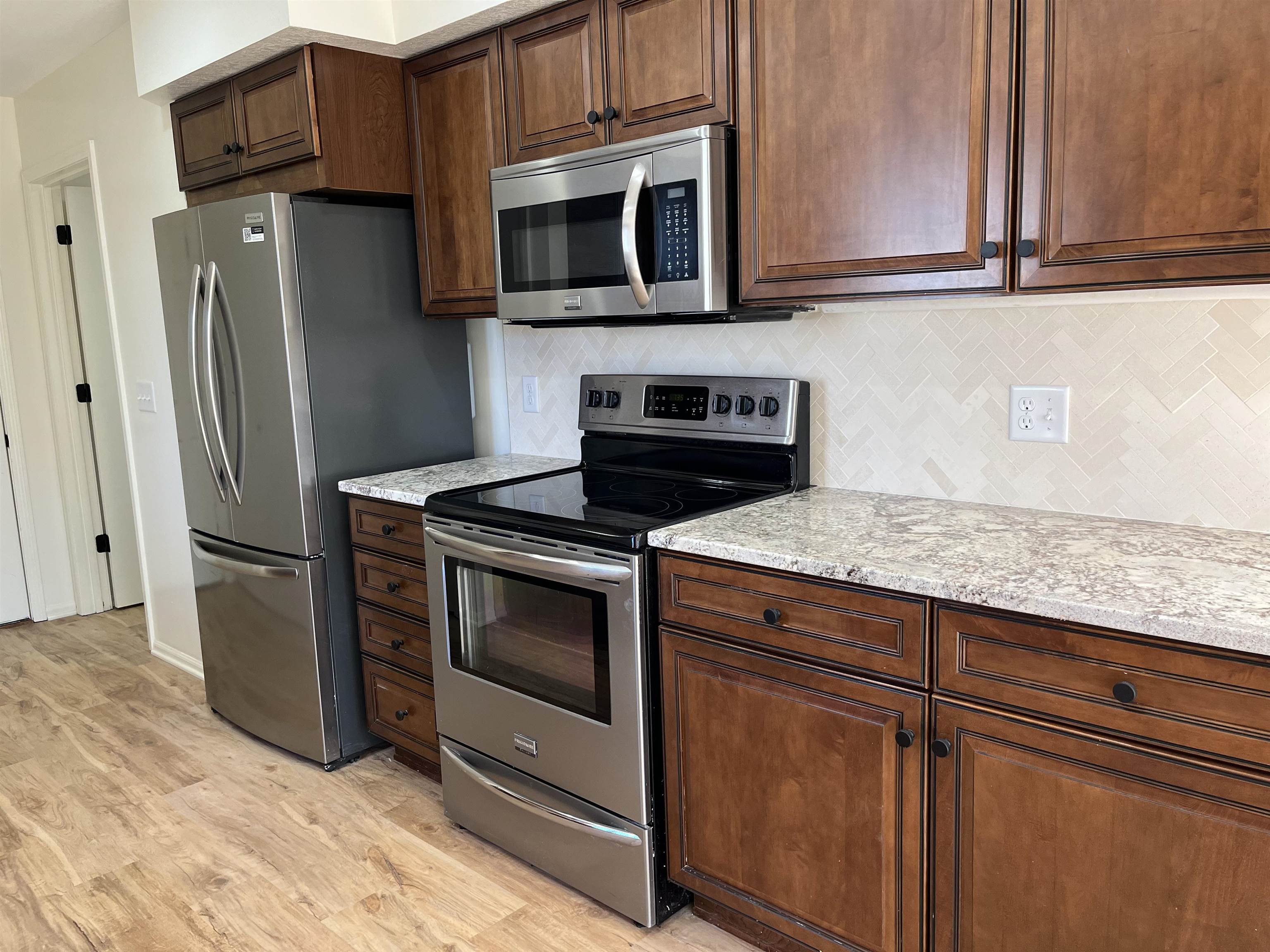 Kitchen with stainless steel appliances, light stone counters, backsplash, and light wood-style flooring