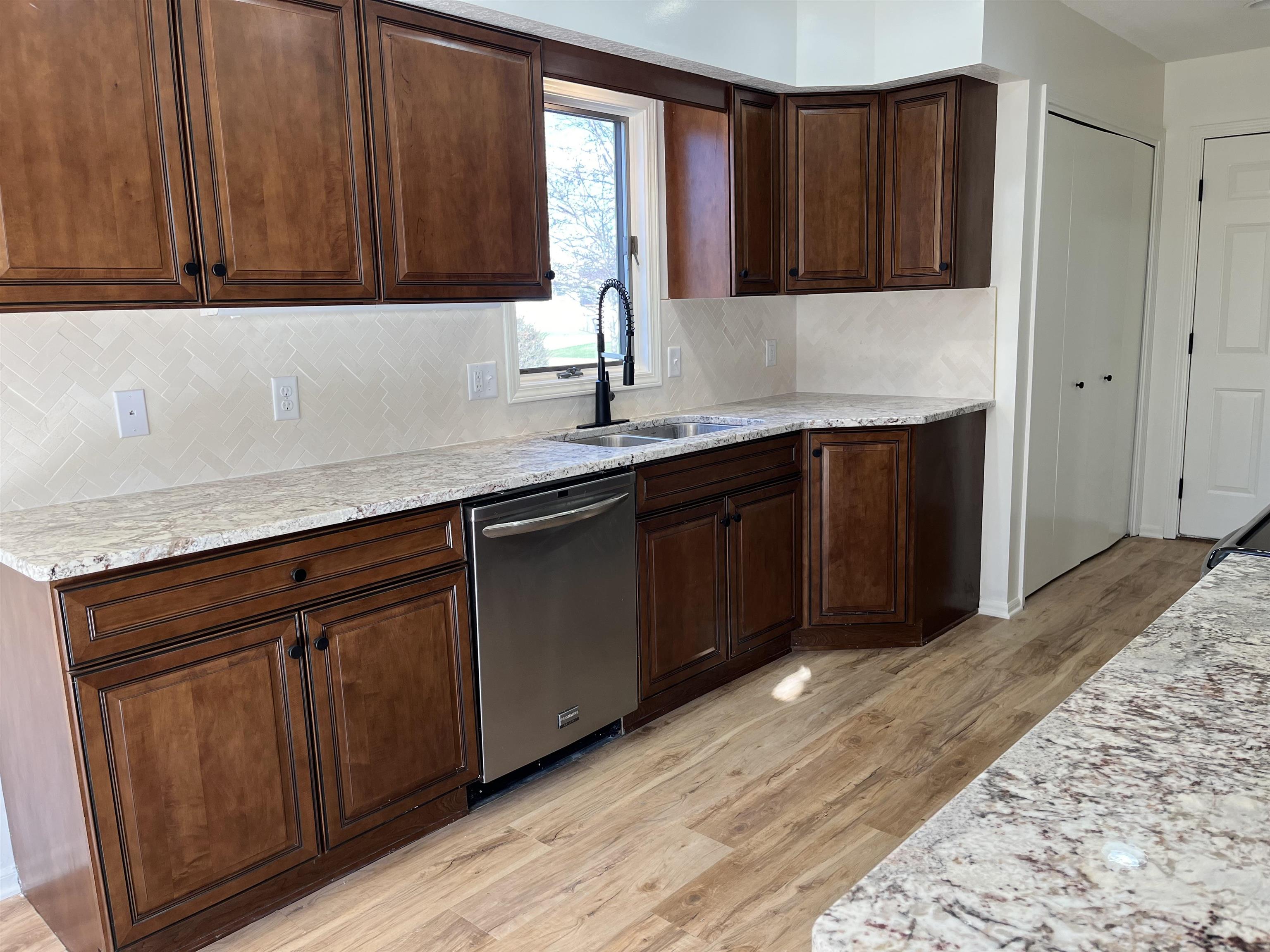Kitchen with stainless steel dishwasher, light wood-style floors, light stone countertops, and dark wood finish cabinetry