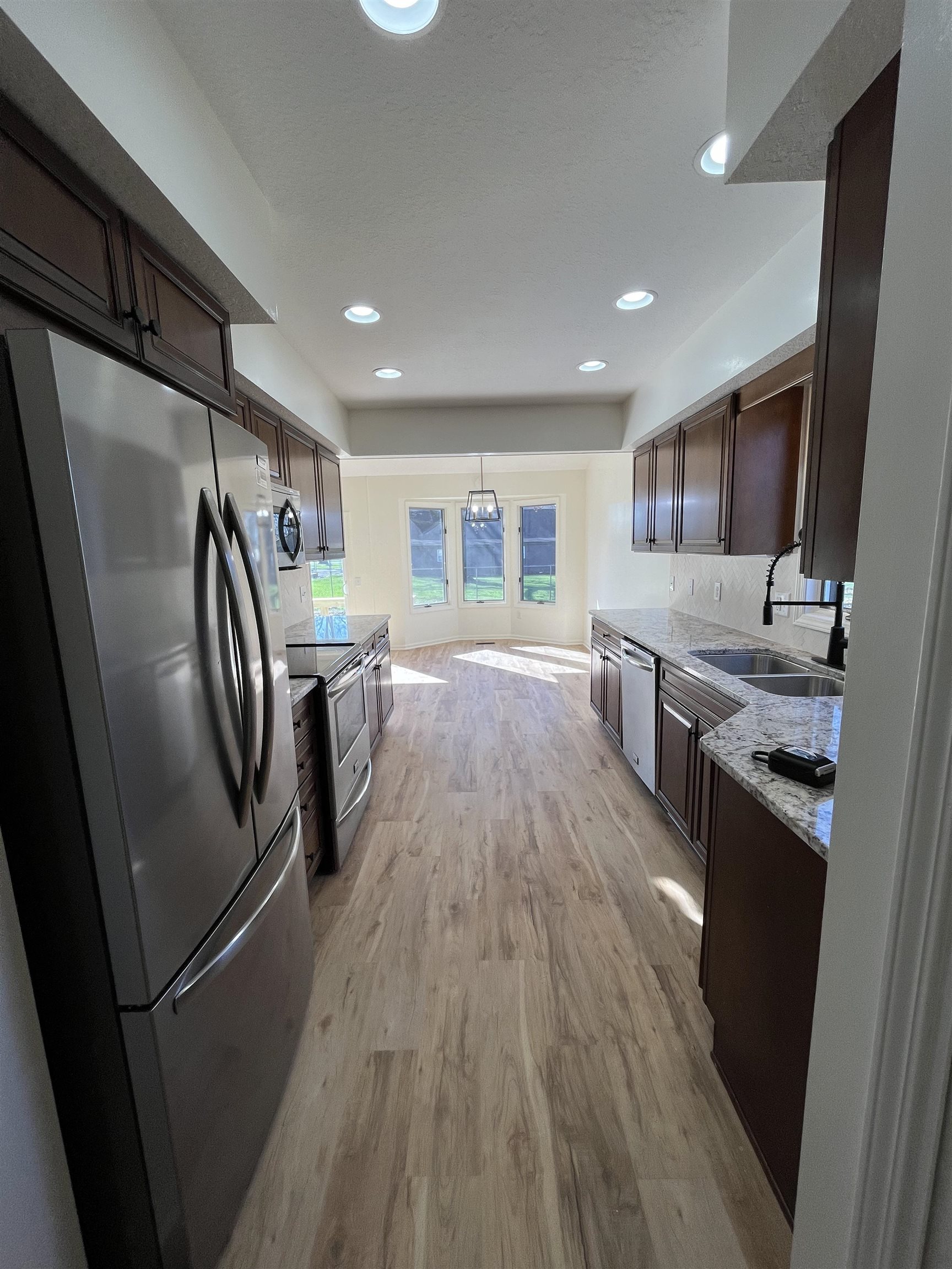 Kitchen featuring stainless steel appliances, dark wood finish cabinets, light stone countertops, and light wood finished floors