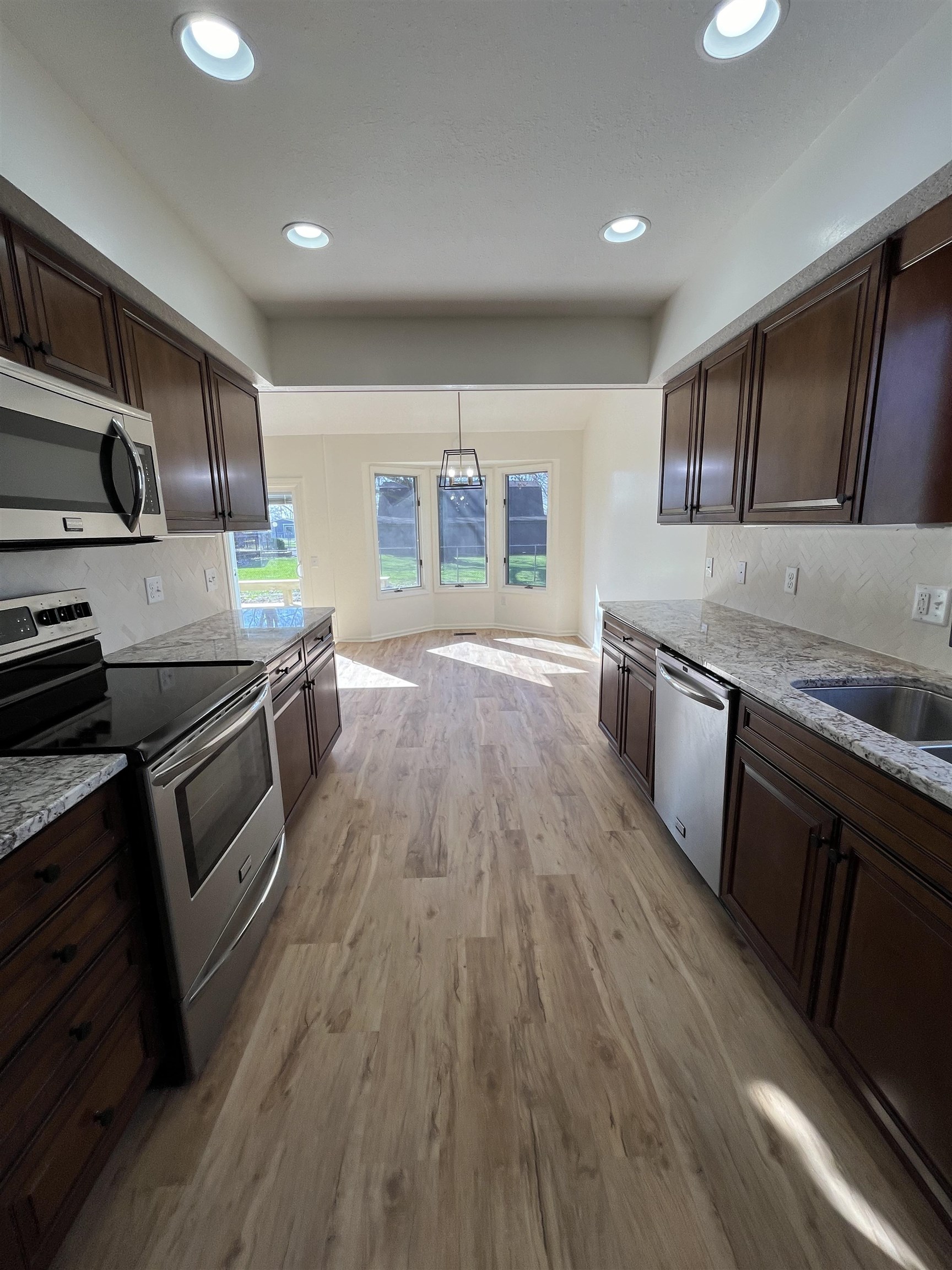 Kitchen with dark wood finish cabinetry, stainless steel appliances, light stone counters, and light wood finished floors