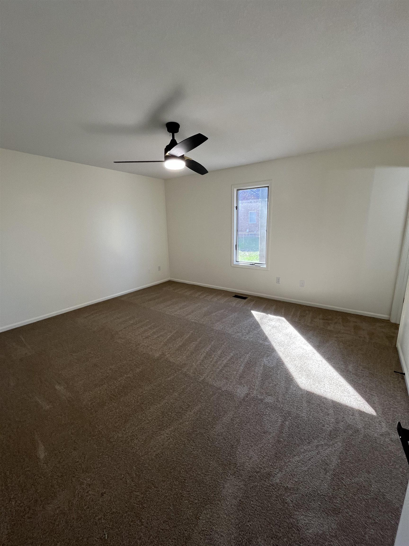 Empty room featuring dark carpet and ceiling fan