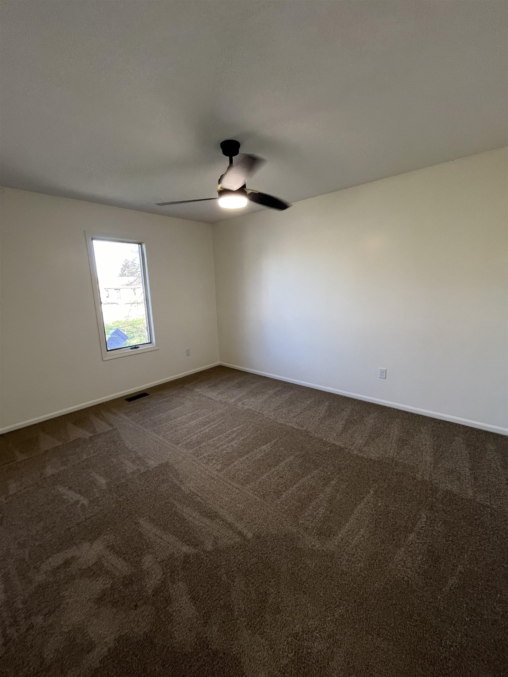 Empty room featuring dark carpet and a ceiling fan