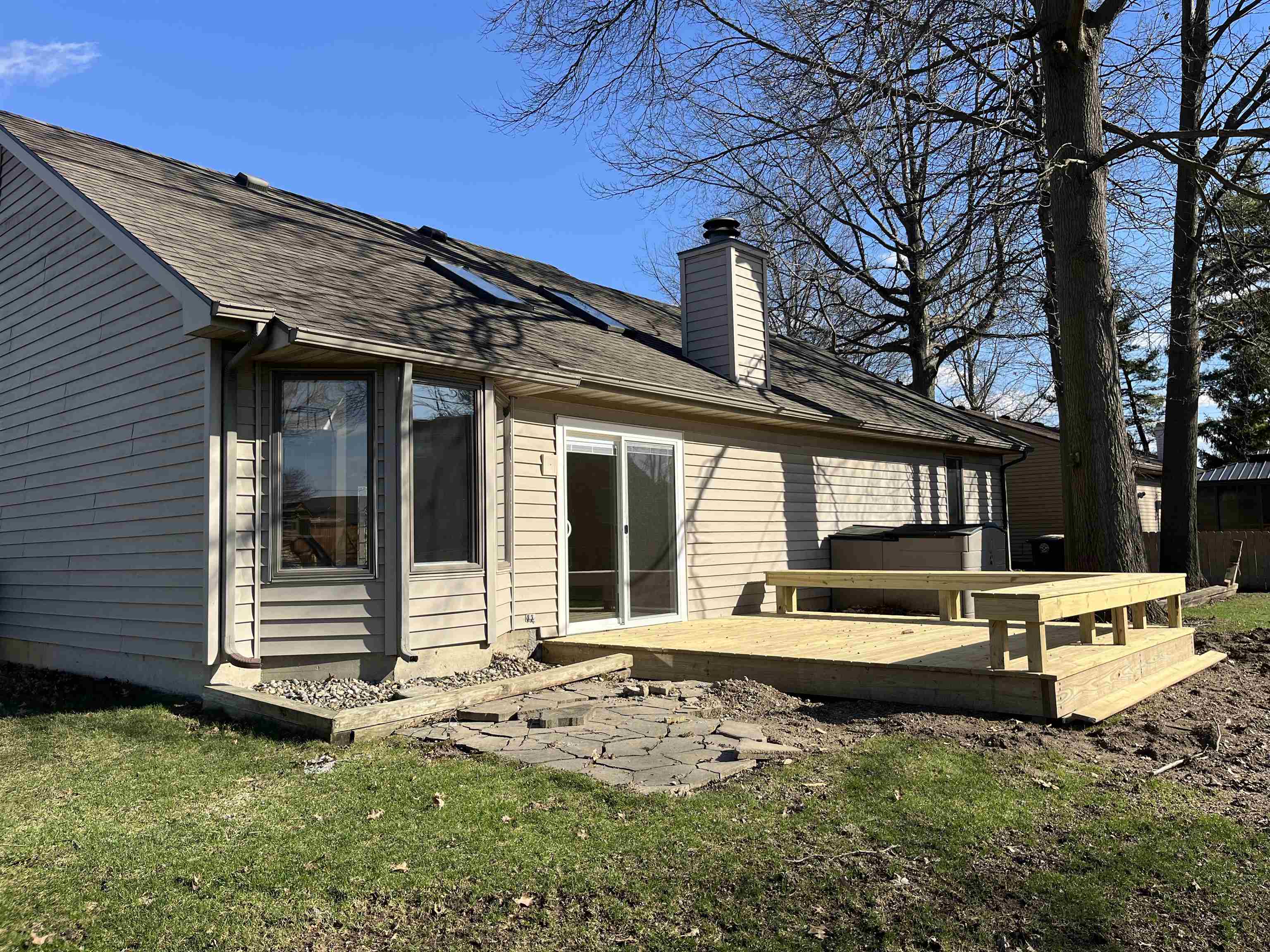 Back of property with a shingled roof, a chimney, a lawn, a deck, and a jacuzzi