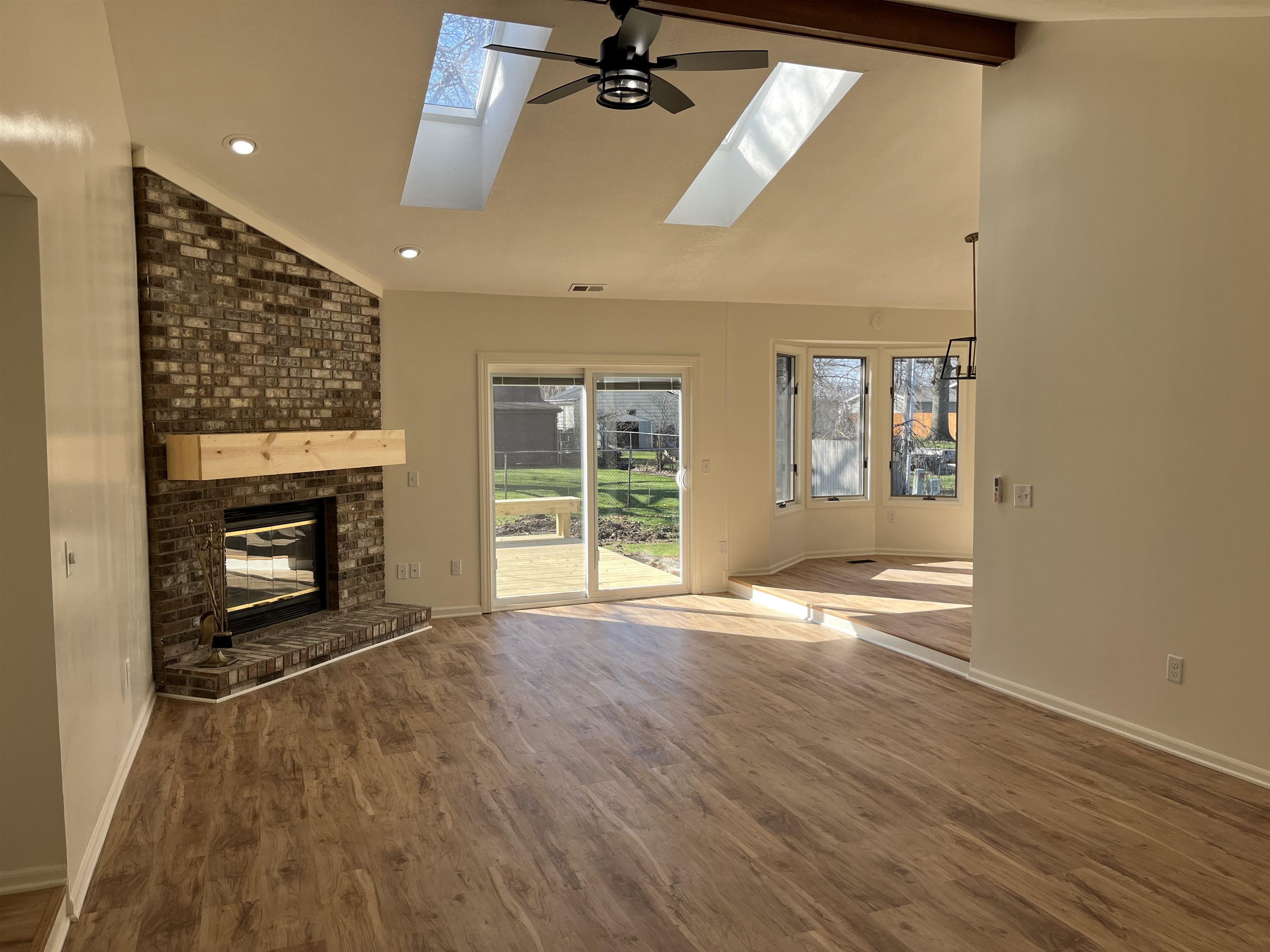 Unfurnished living room with vaulted ceiling, a brick fireplace, dark wood-style flooring, a skylight, and plenty of natural light