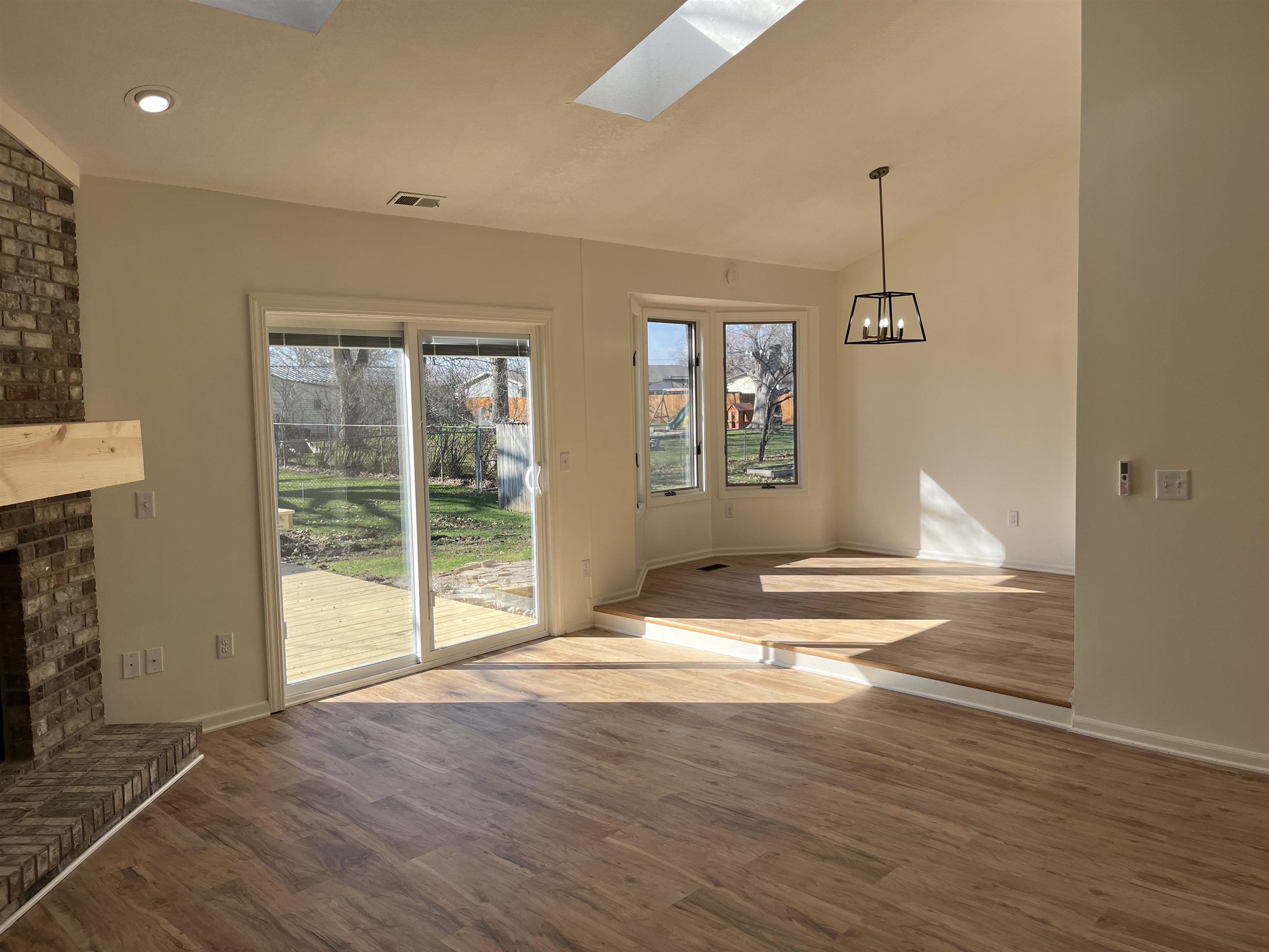 Unfurnished dining area featuring a fireplace, a skylight, lofted ceiling, wood finished floors, and a chandelier