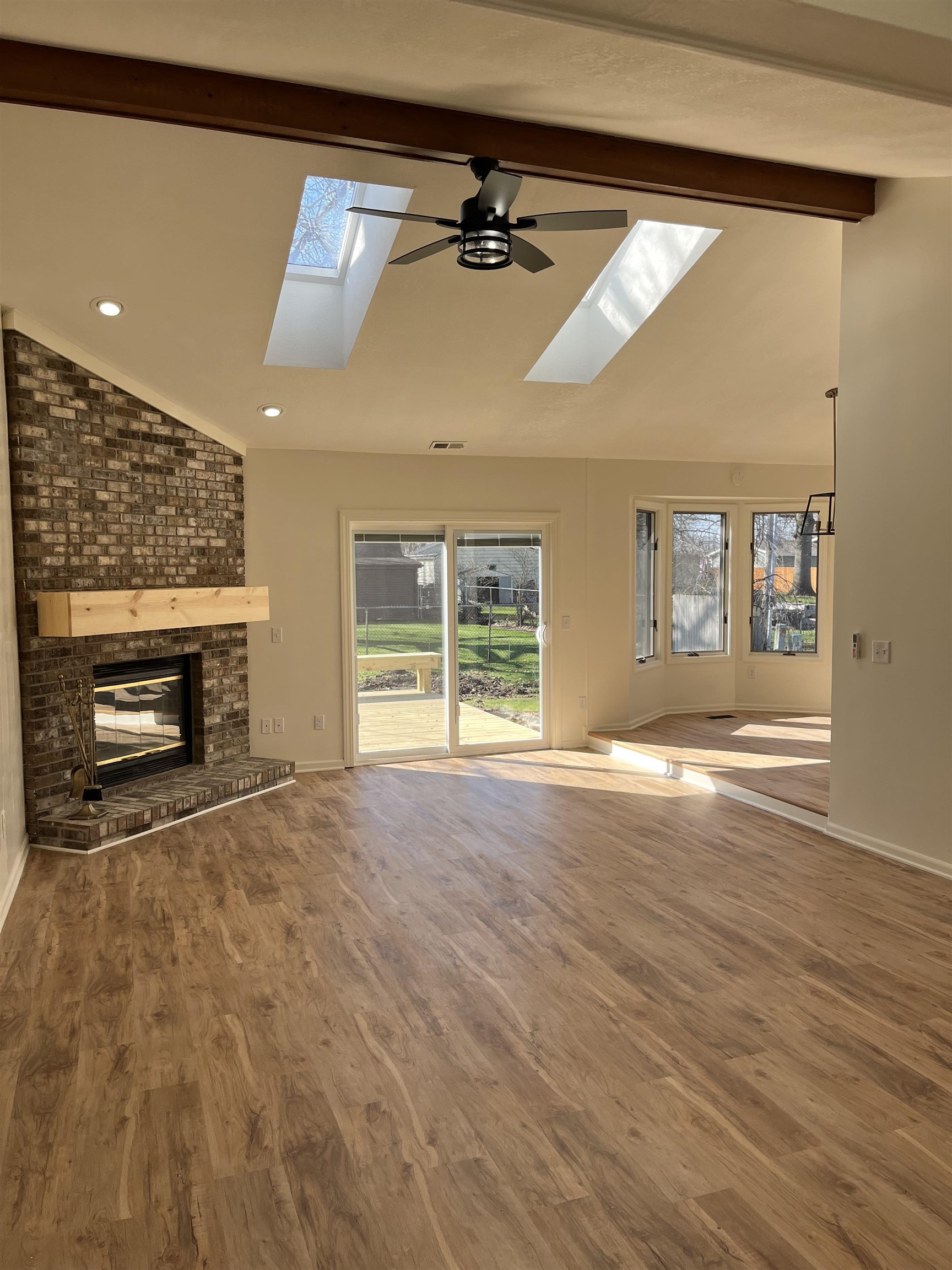 Unfurnished living room with lofted ceiling, a fireplace, a ceiling fan, a skylight, and wood finished floors