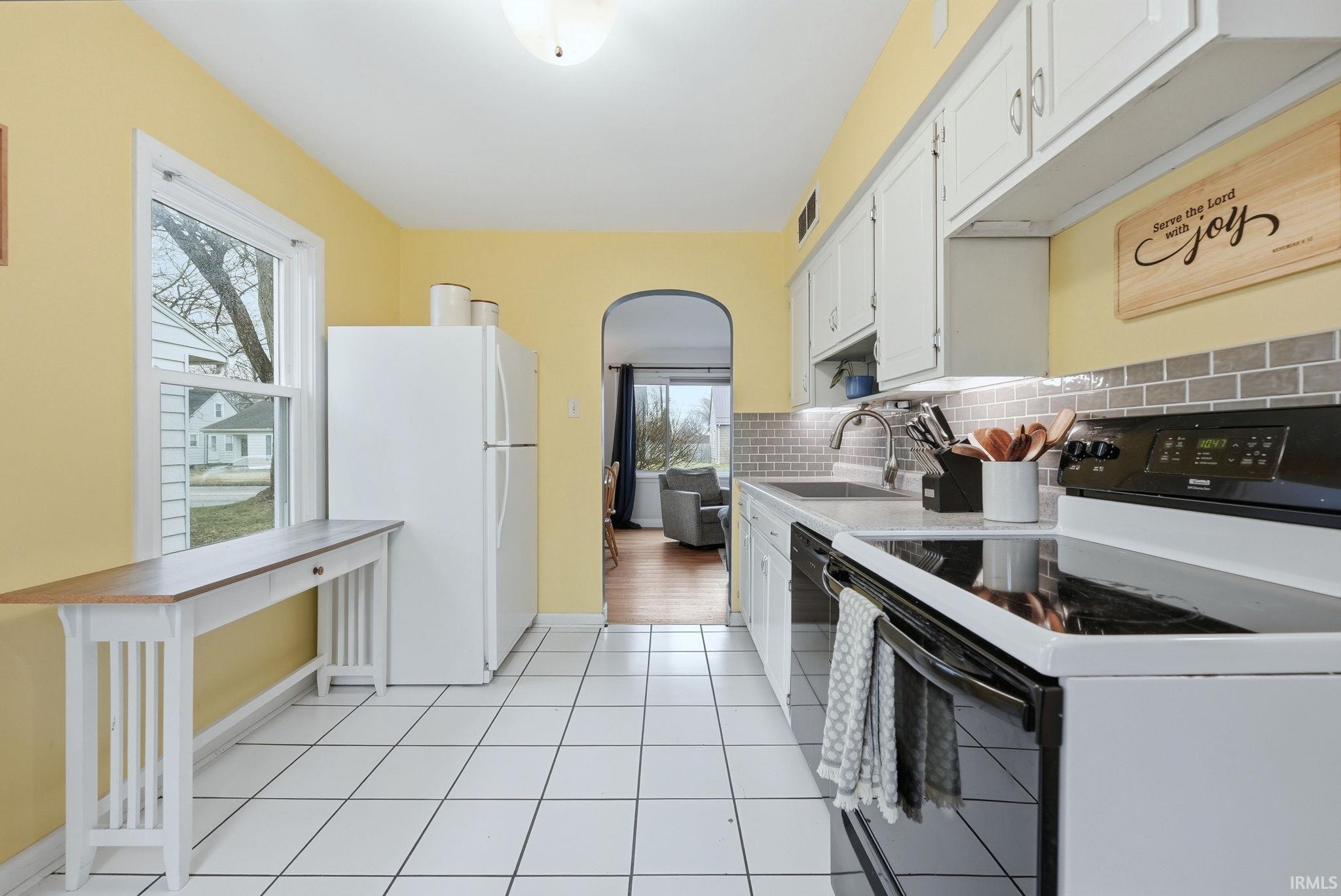 Kitchen with black appliances, light countertops, arched walkways, white cabinets, and light tile patterned flooring