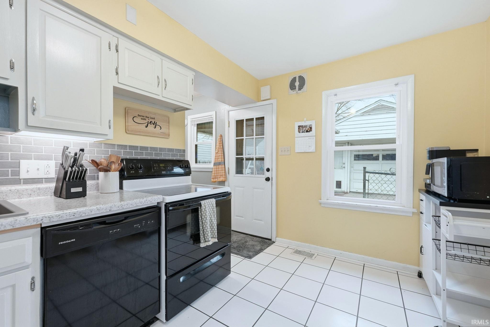 Kitchen featuring black appliances, backsplash, white cabinetry, light countertops, and light tile patterned floors
