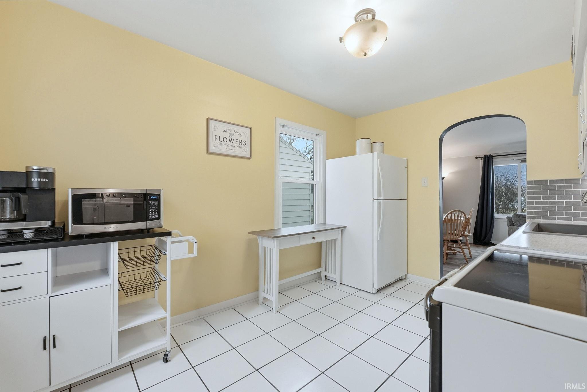 Kitchen with white appliances, white cabinetry, arched walkways, and decorative backsplash